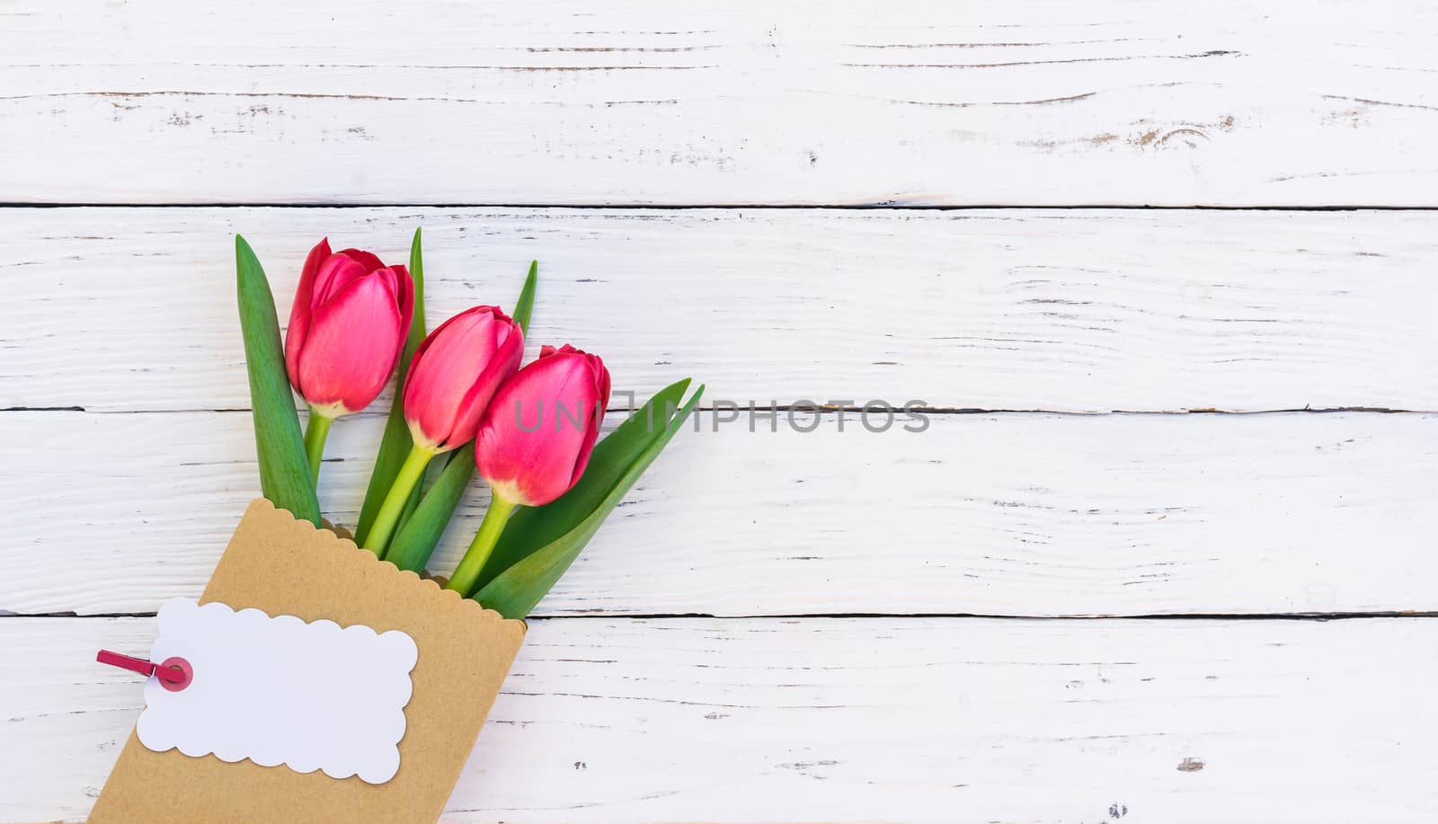 Bouquet of red tulip spring flowers with empty label on white wooden background