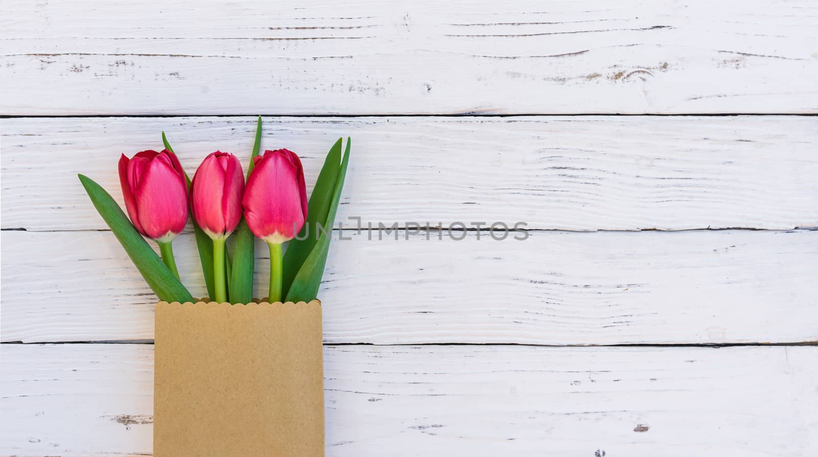 Fresh red tulips in paper bag on white wooden background with copy space
