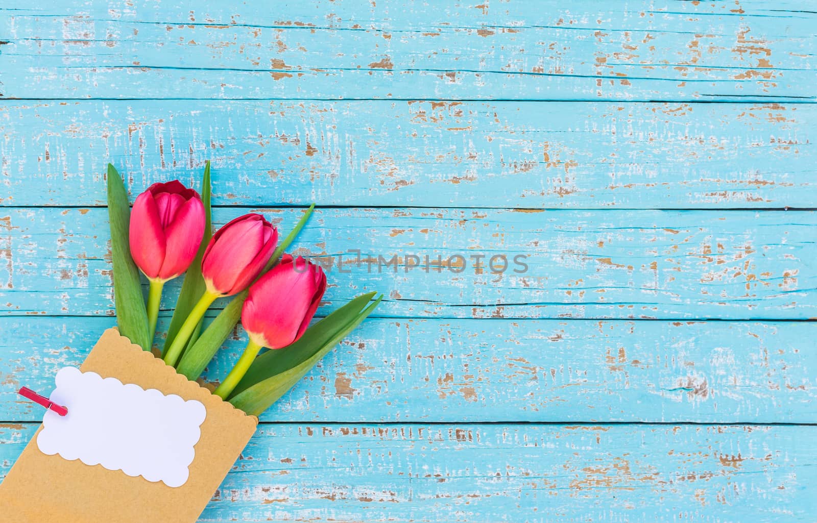Bunch of red tulips in paper bag with blank label on blue wooden background