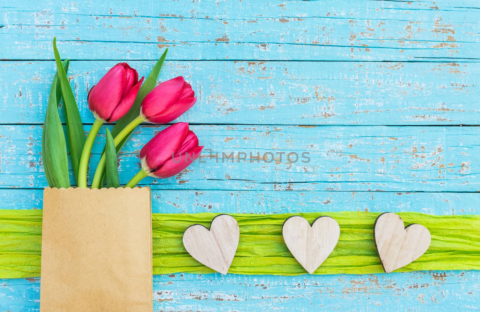 Bunch of flowers with red tulips and hearts border on blue wood with copy space