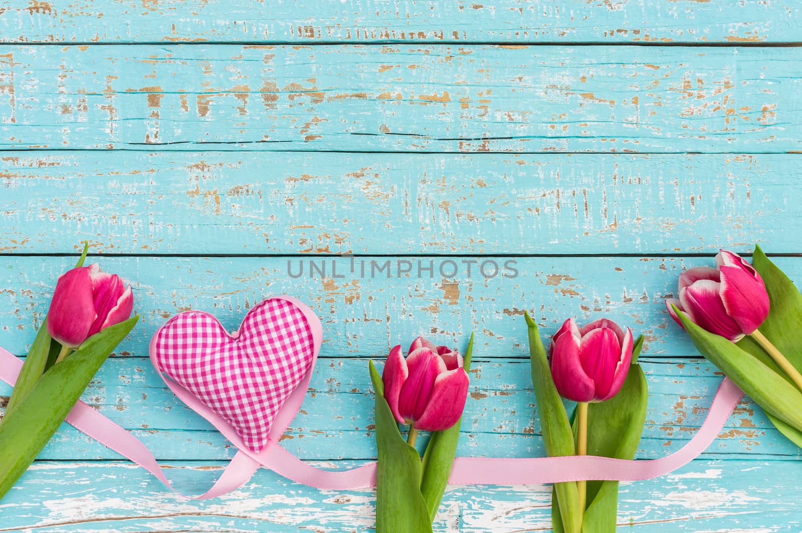 Romantic frame of pink heart with tulips on blue wooden background with copy space