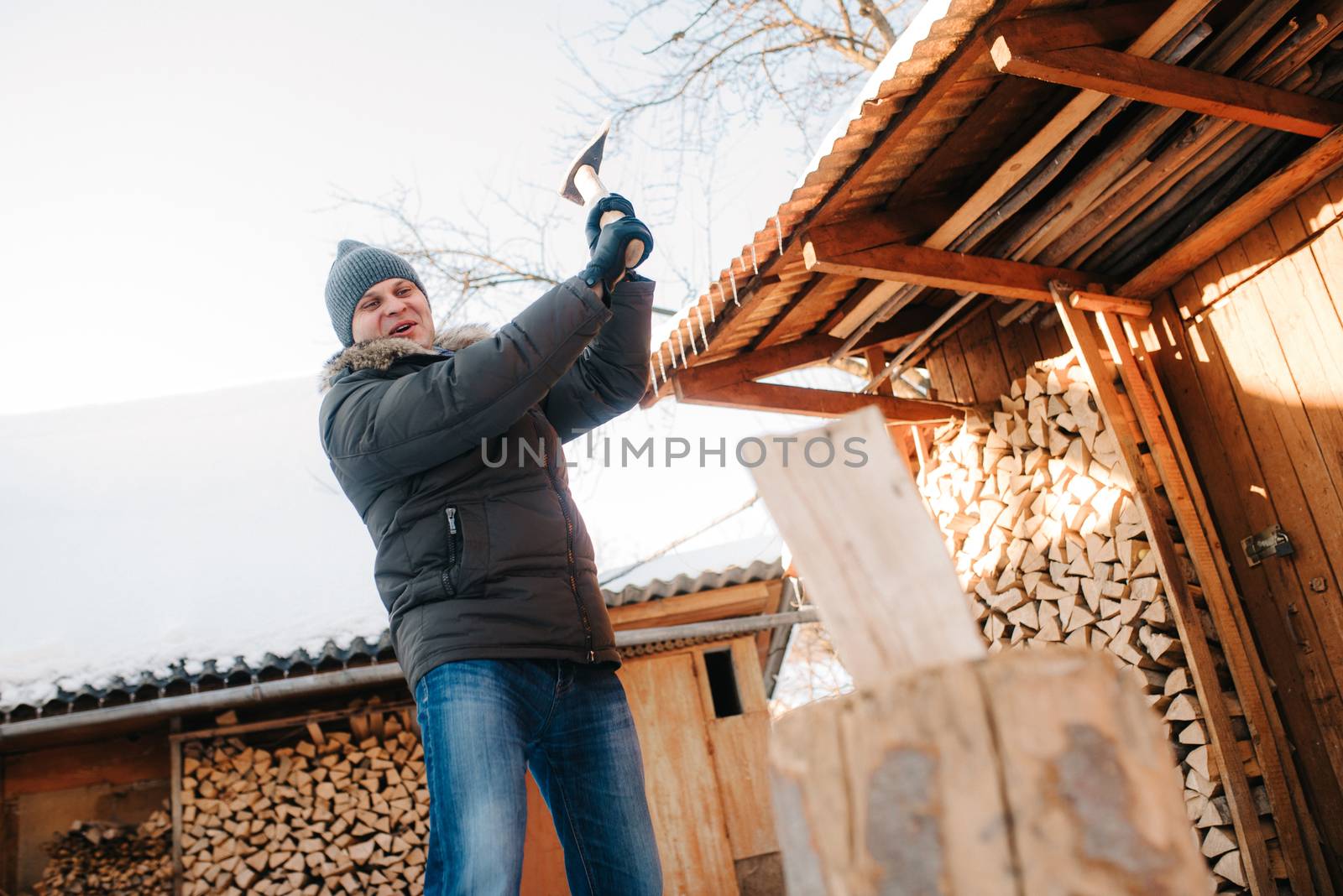 guy in winter clothes chopping wood in the yard, covered with snow