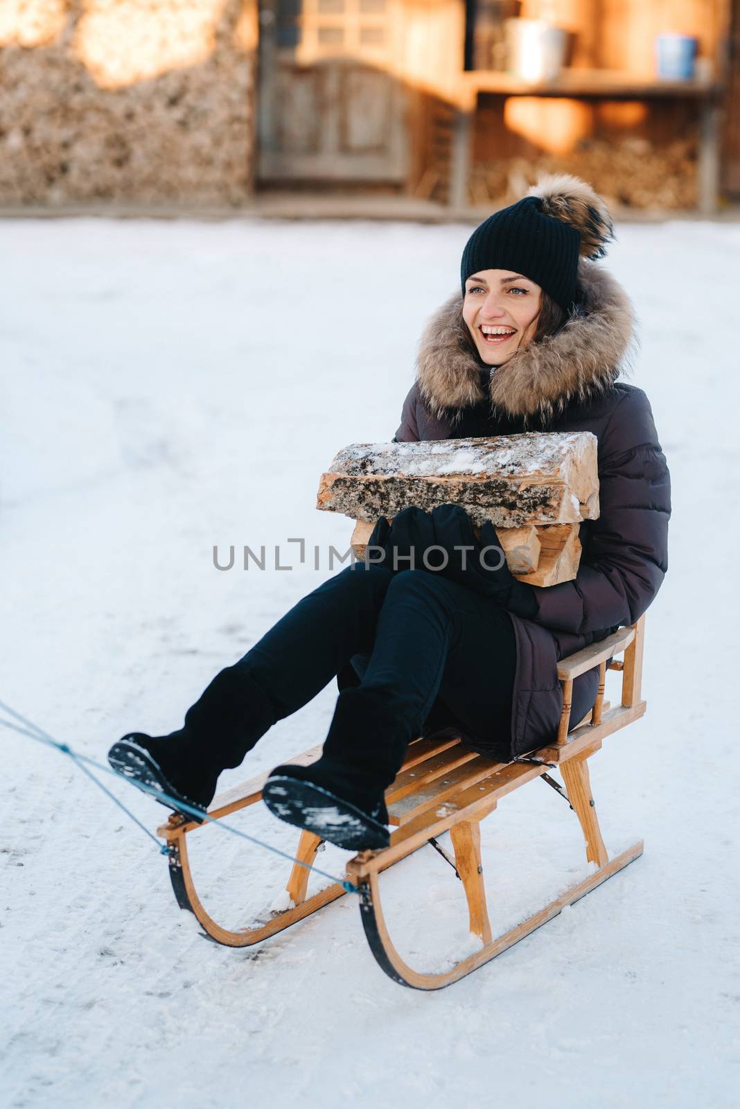 girl sitting in a sled, smiling and holding a wooden log in her hands