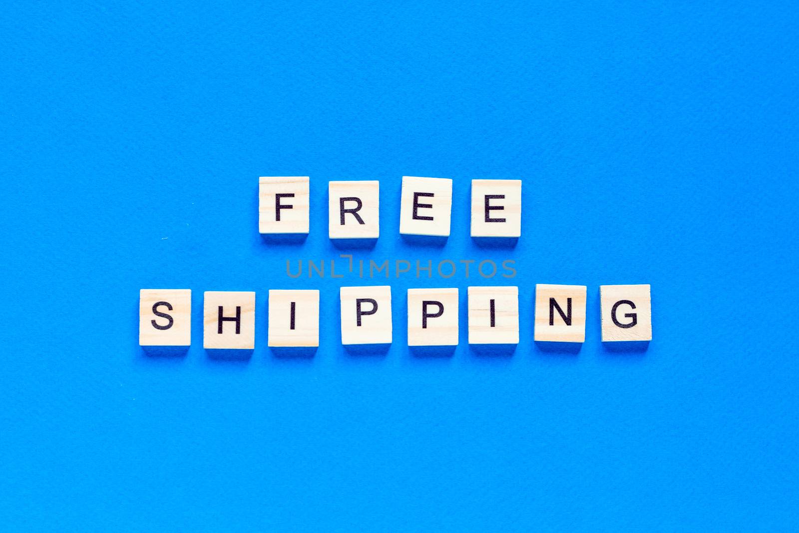 free shipping lettering in wooden letters on a blue background, top view. Service concept, delivery, contactless delivery, promotion, free of charge.