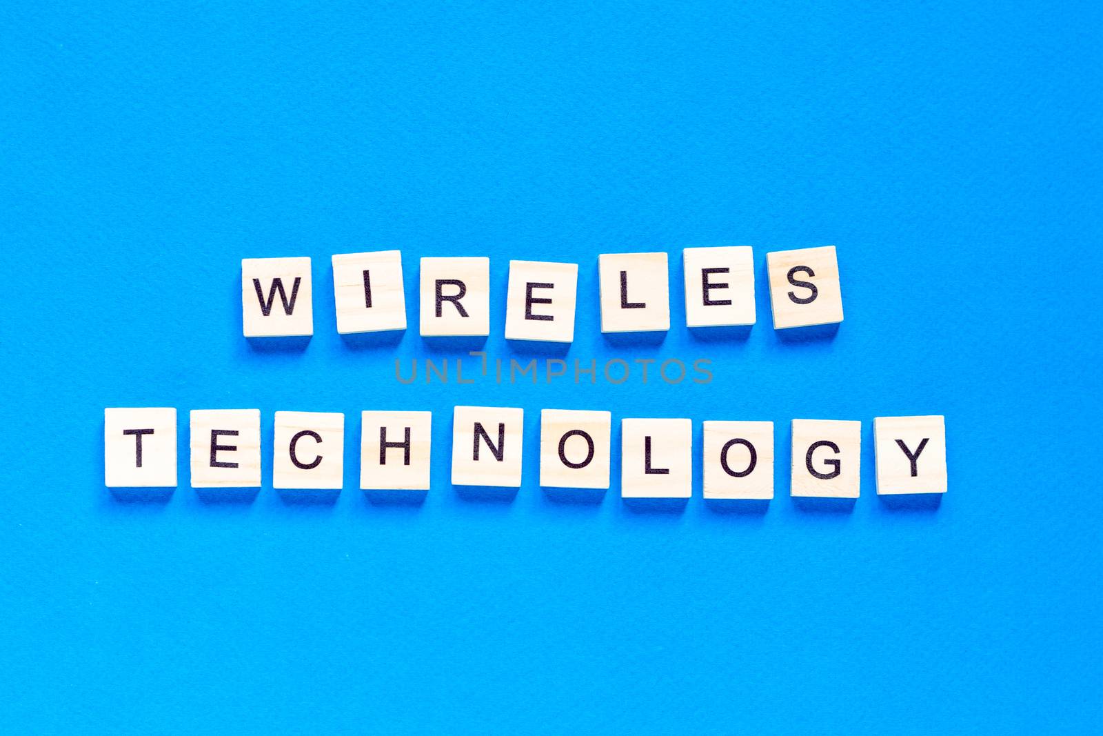 The words wireless technology, spelt with wooden letter tiles over a white background. wireless technology lettering in wooden letters by Pirlik