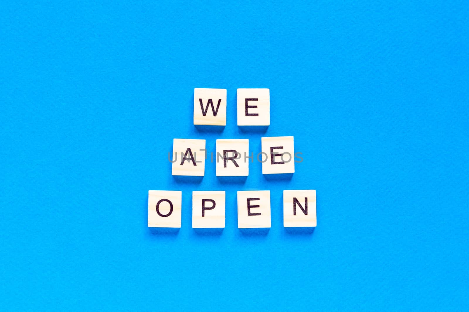 We are open. Wooden cubes with a text message We are open on a blue background. The view from the top. Flat layout. An office, cafe, or store welcomes guests after a coronavirus outbreak. by Pirlik