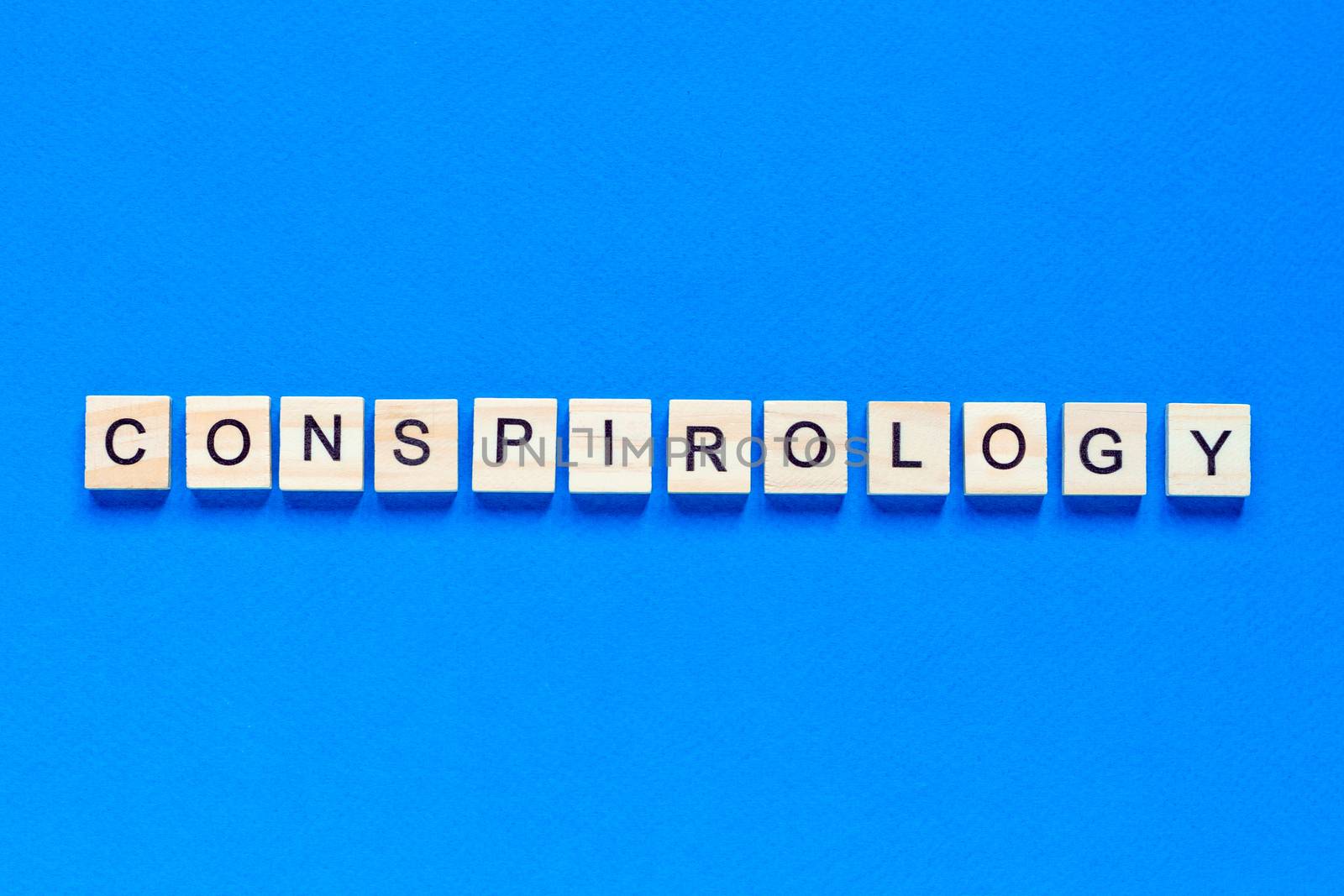 Conspirology - words made of wooden blocks with letters, secret plan of powerful people, conspiracy theory concept, top view blue background.