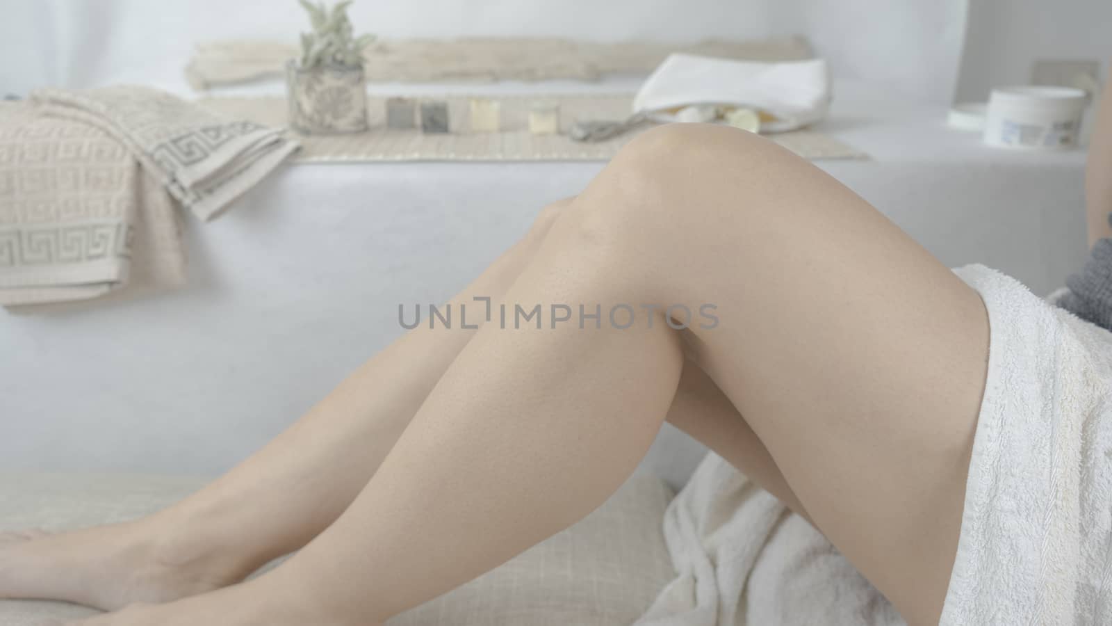 Bare legs of a woman in white towel sitting in her modern spa design bathroom by robbyfontanesi