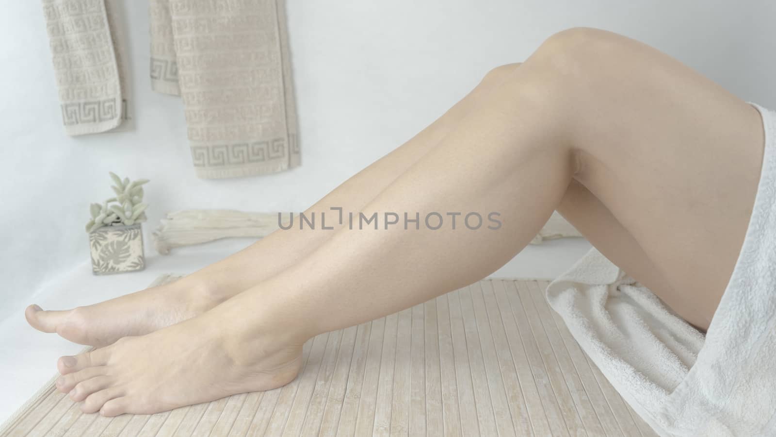 Bare legs of a woman in white towel sitting in her modern spa design bathroom