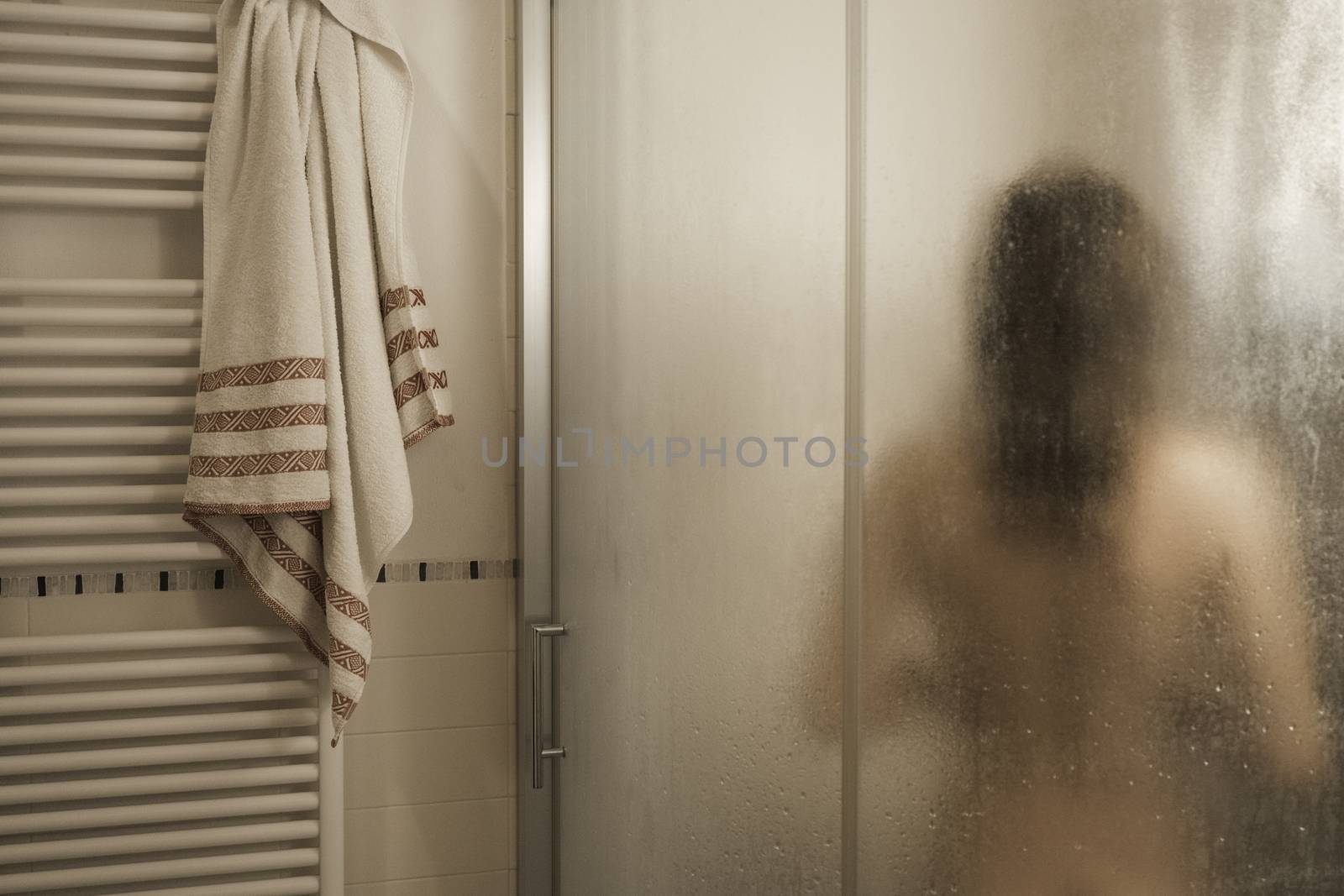 Sexy naked brunette woman take a shower inside the shower cabin seen through foggy glass in her modern design bathroom