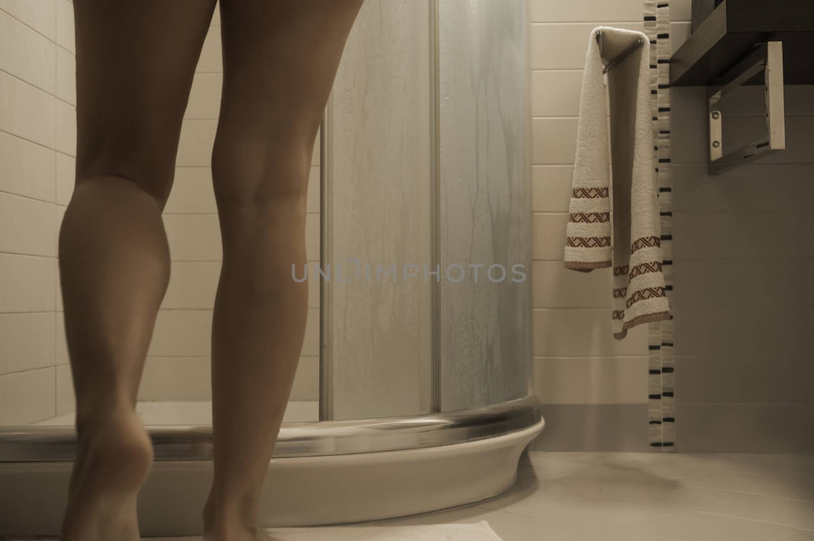 Sexy naked woman's legs entering the foggy glass shower cabin in her modern design bathroom