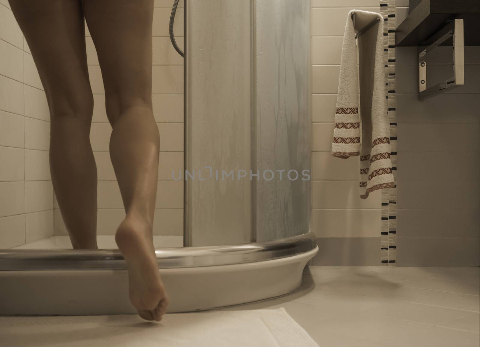 Sexy naked woman's legs entering the foggy glass shower cabin in her modern design bathroom