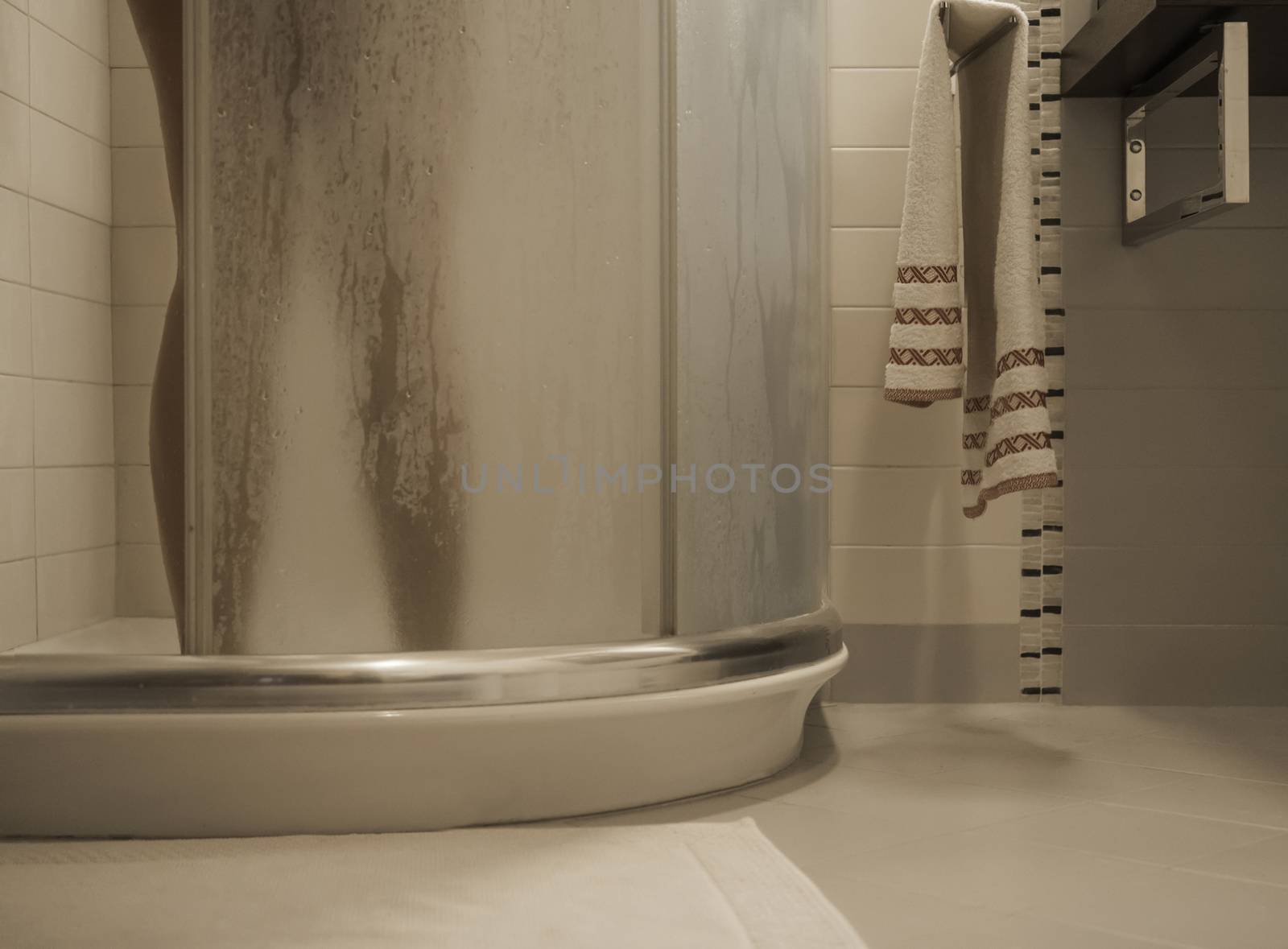 Sexy naked woman's legs inside the shower cabin closes the fogged glass door in her modern design bathroom