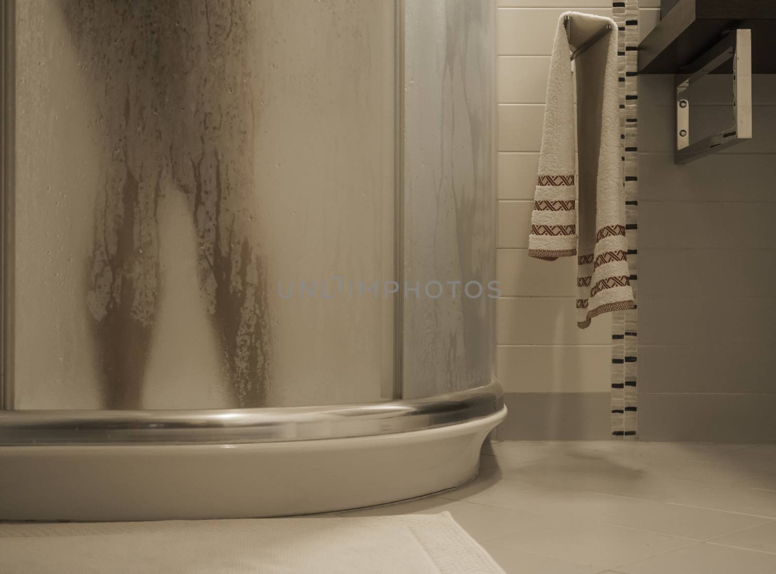 Sexy naked woman's legs inside the shower cabin behind the fogged glass door in her modern design bathroom