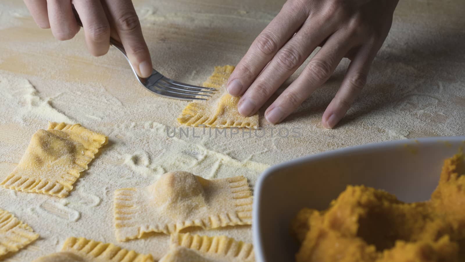 Closeup process making ravioli vegan homemade pasta. Housewife cook closes with a fork 'tortelli di zucca', traditional italian pasta, woman cooking food on kitchen