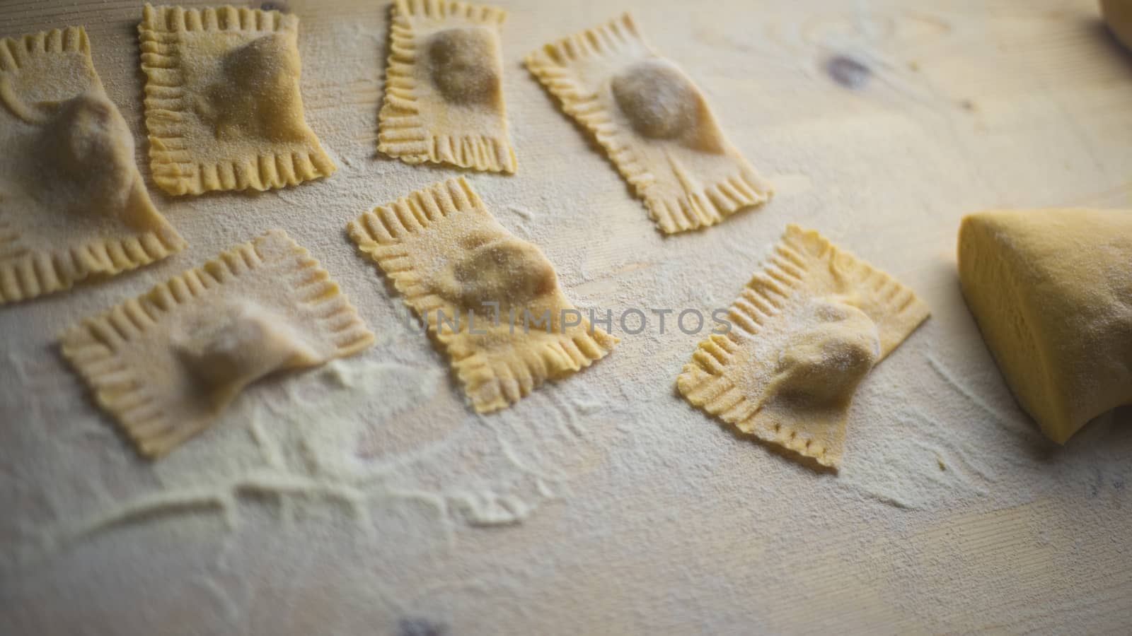 Closeup of pumpkin ravioli vegan, traditional Italian pasta, homemade pasta just made, with the dough mass durum wheat flour and wheat flour scattered on the light wooden table