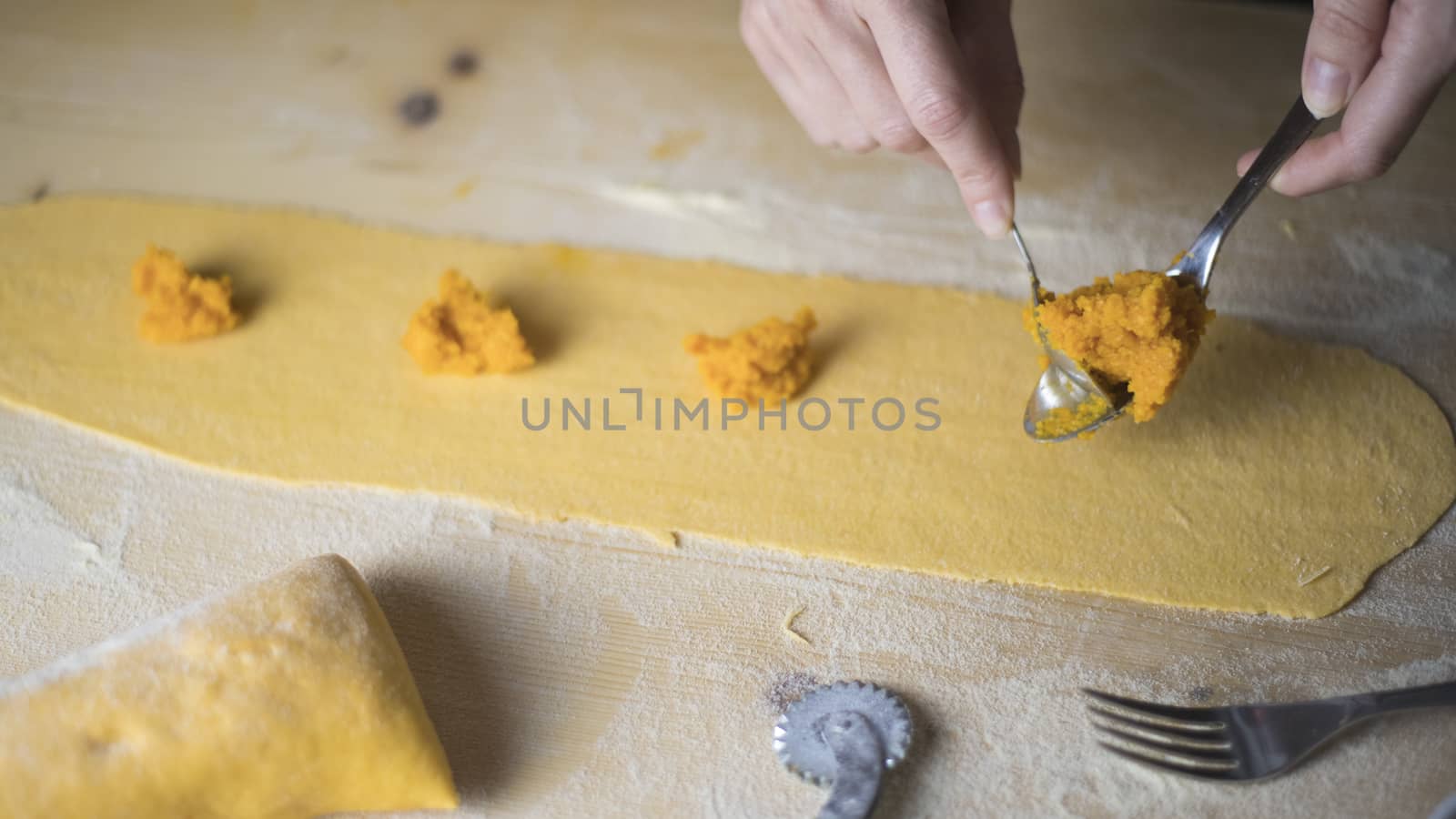 Closeup process making ravioli vegan homemade pasta. Housewife cook place the filling of the 'tortelli di zucca' on the pastry, measuring it with a spoon, on light wooden table by robbyfontanesi
