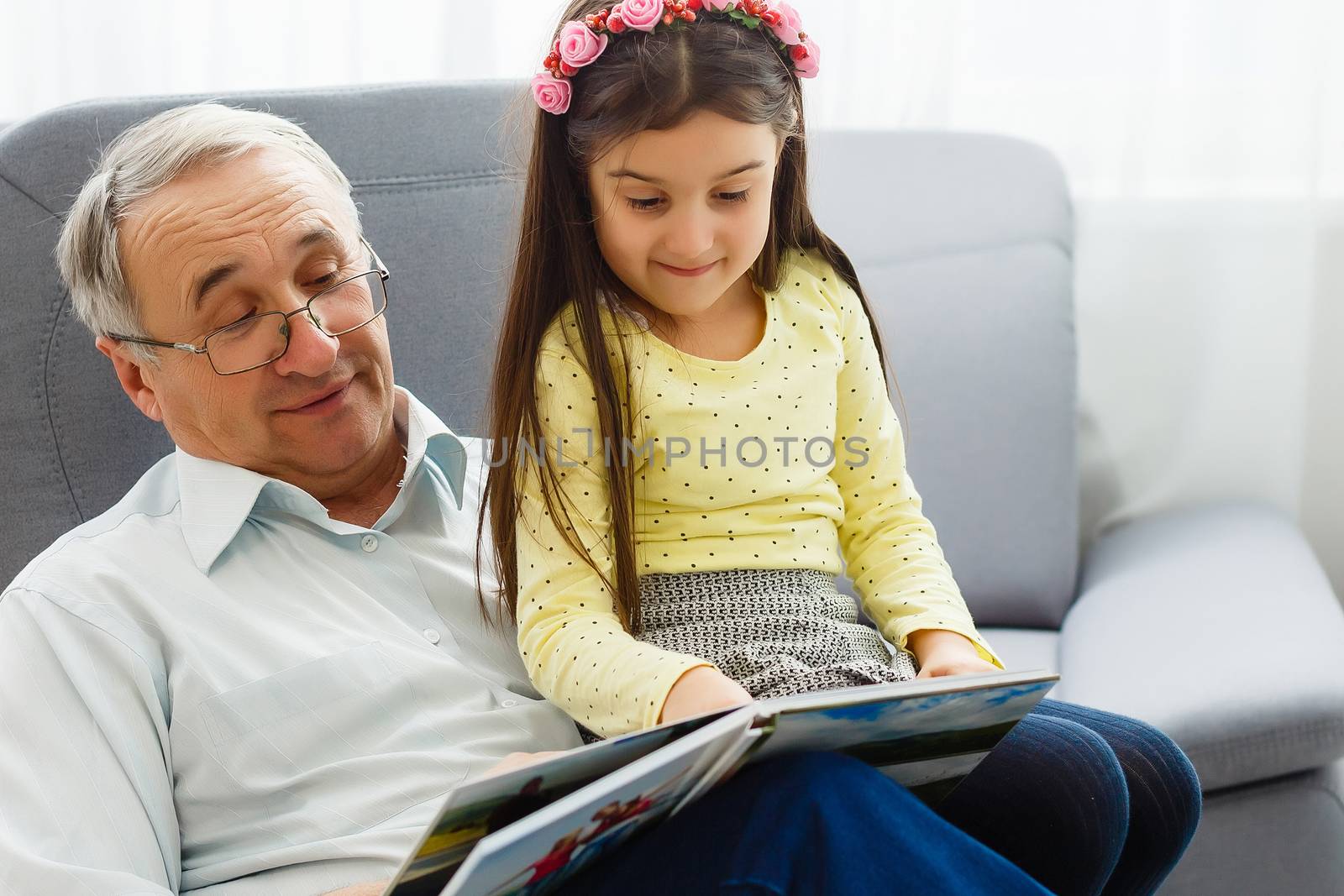 Granddaughter and grandfather watching photos together in a photo album at home by Andelov13