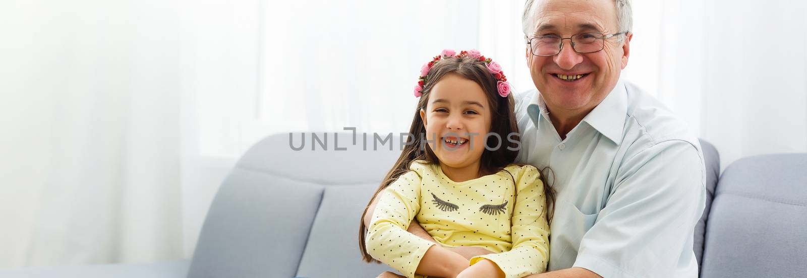 The happy girl hugs a grandfather on the sofa