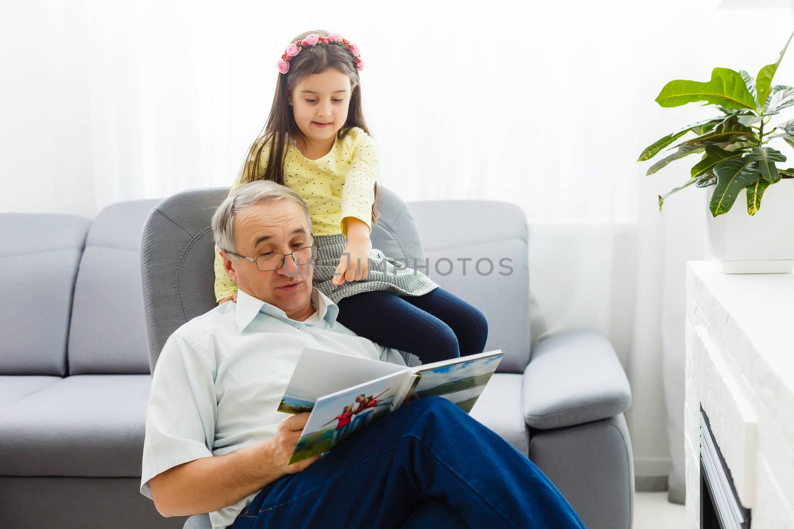 Granddaughter and grandfather watching photos together in a photo album at home by Andelov13