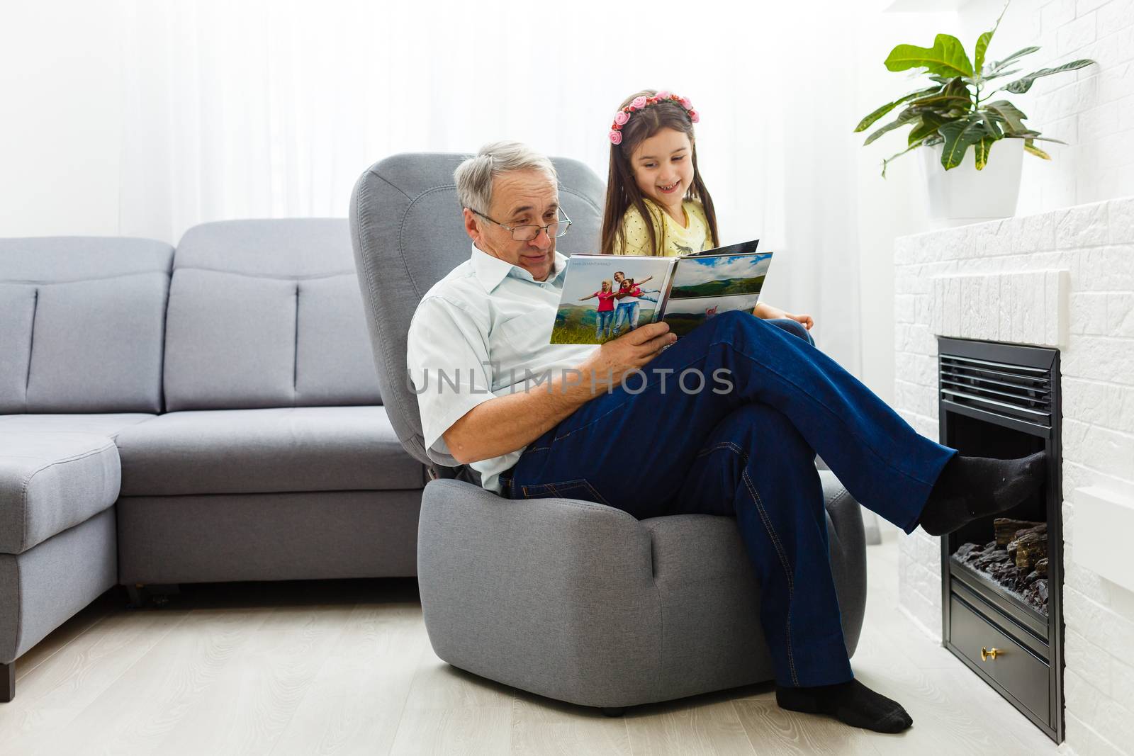 Granddaughter and grandfather watching photos together in a photo album at home by Andelov13