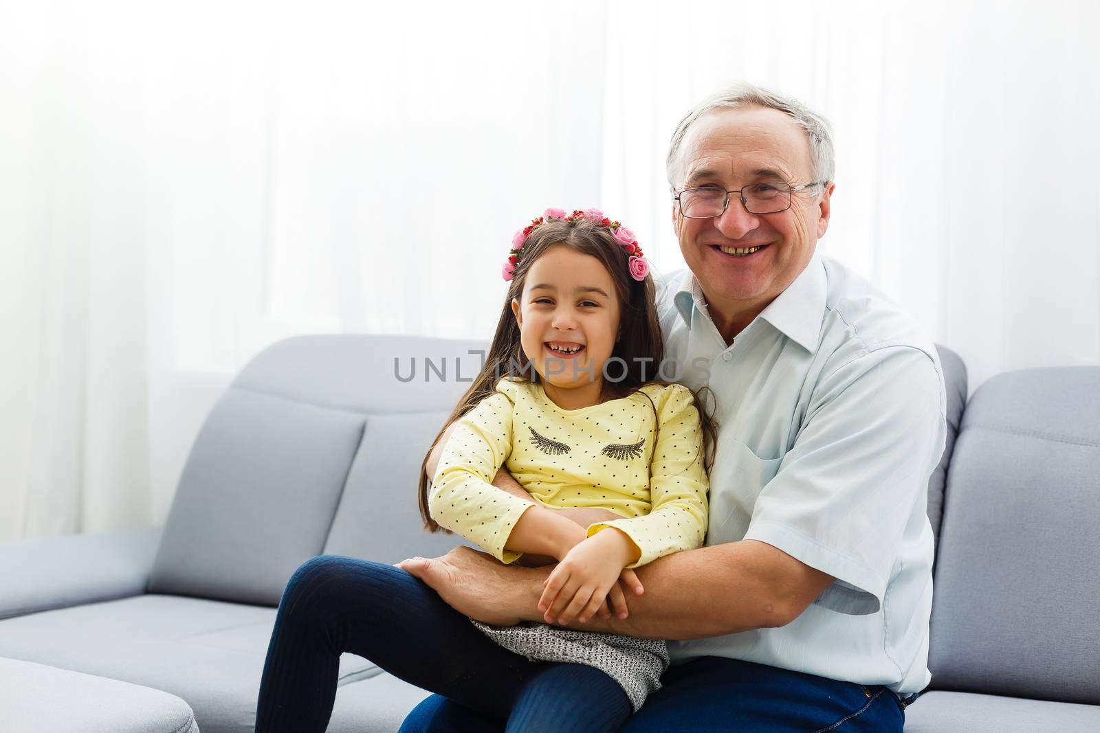 The happy girl hugs a grandfather on the sofa