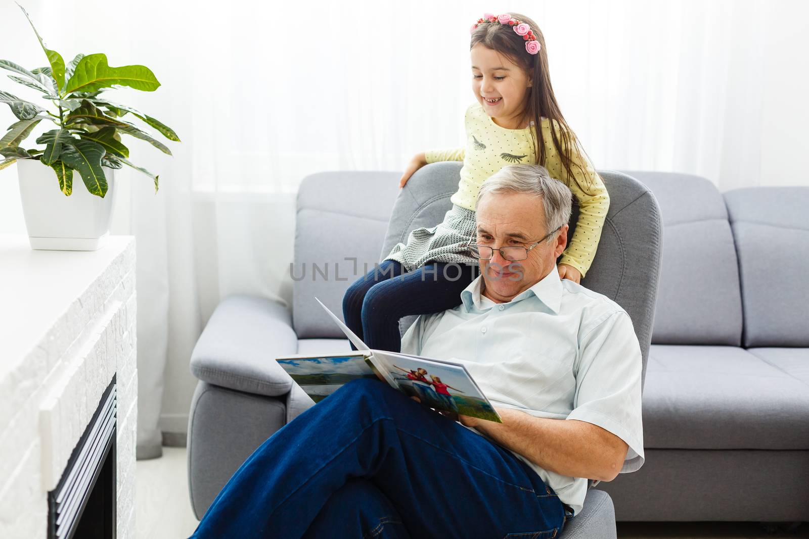 Grandfather and granddaughter on sofa at home. Grandpa and children are watching photos in album.