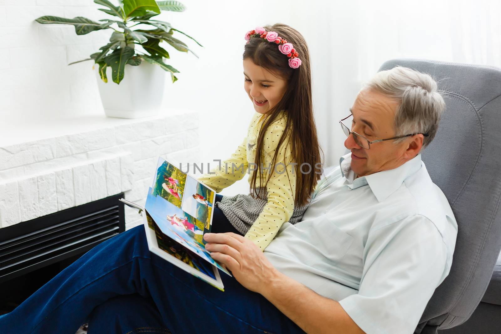 Granddaughter and grandfather watching photos together in a photo album at home by Andelov13