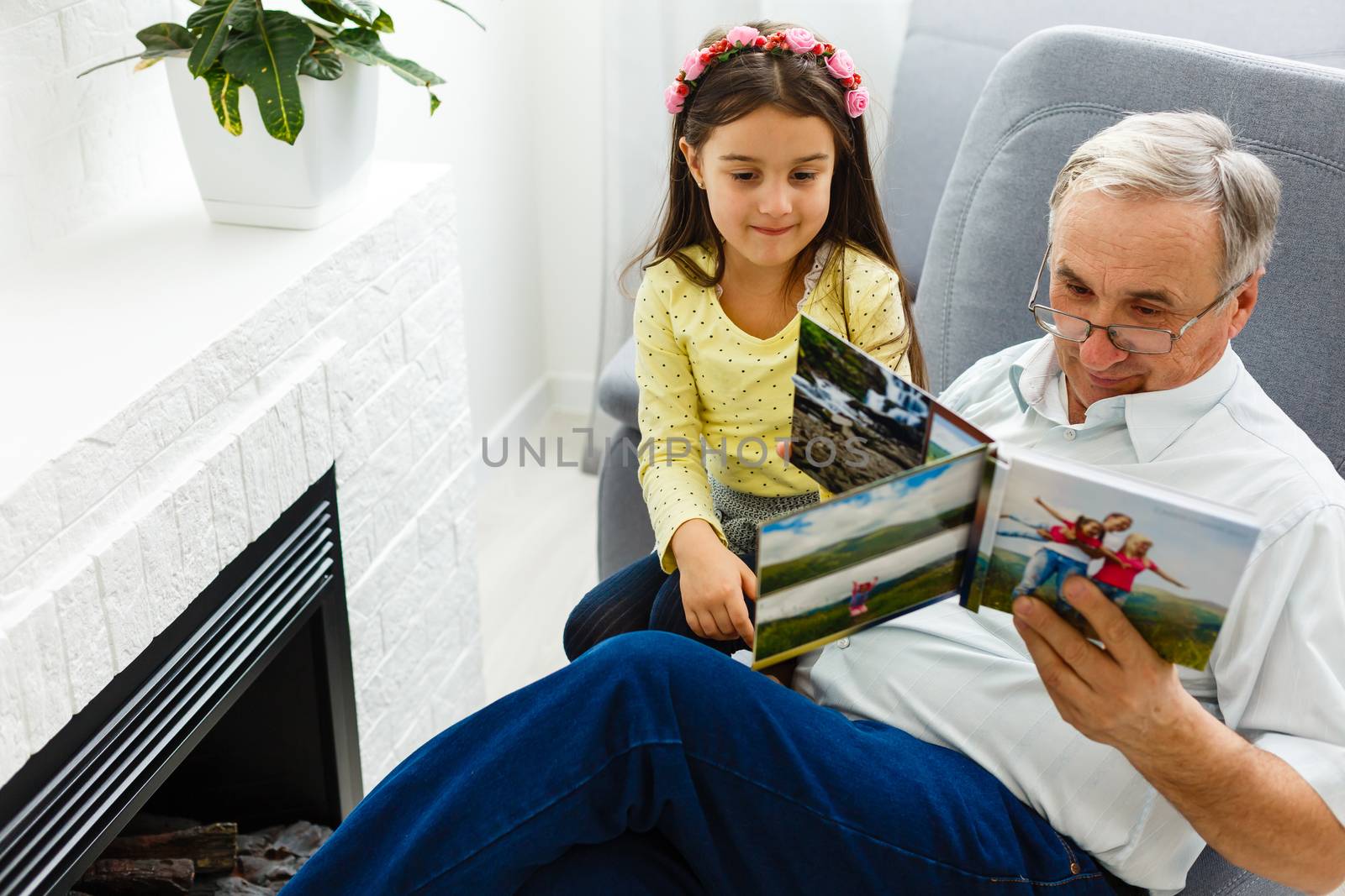 Granddaughter and grandfather watching photos together in a photo album at home by Andelov13