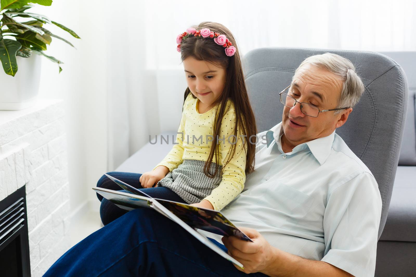 Granddaughter and grandfather watching photos together in a photo album at home by Andelov13