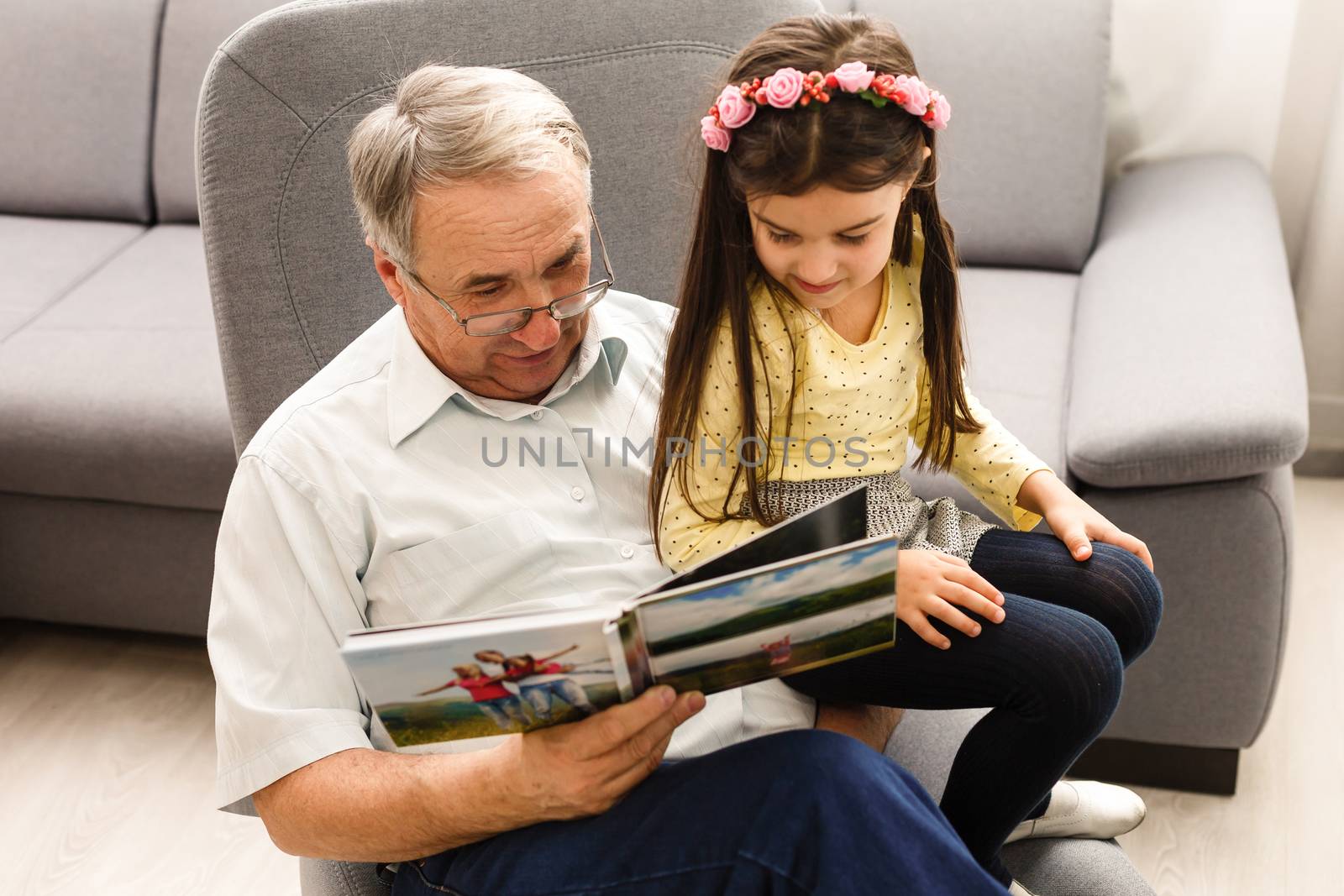 Granddaughter and grandfather watching photos together in a photo album at home by Andelov13