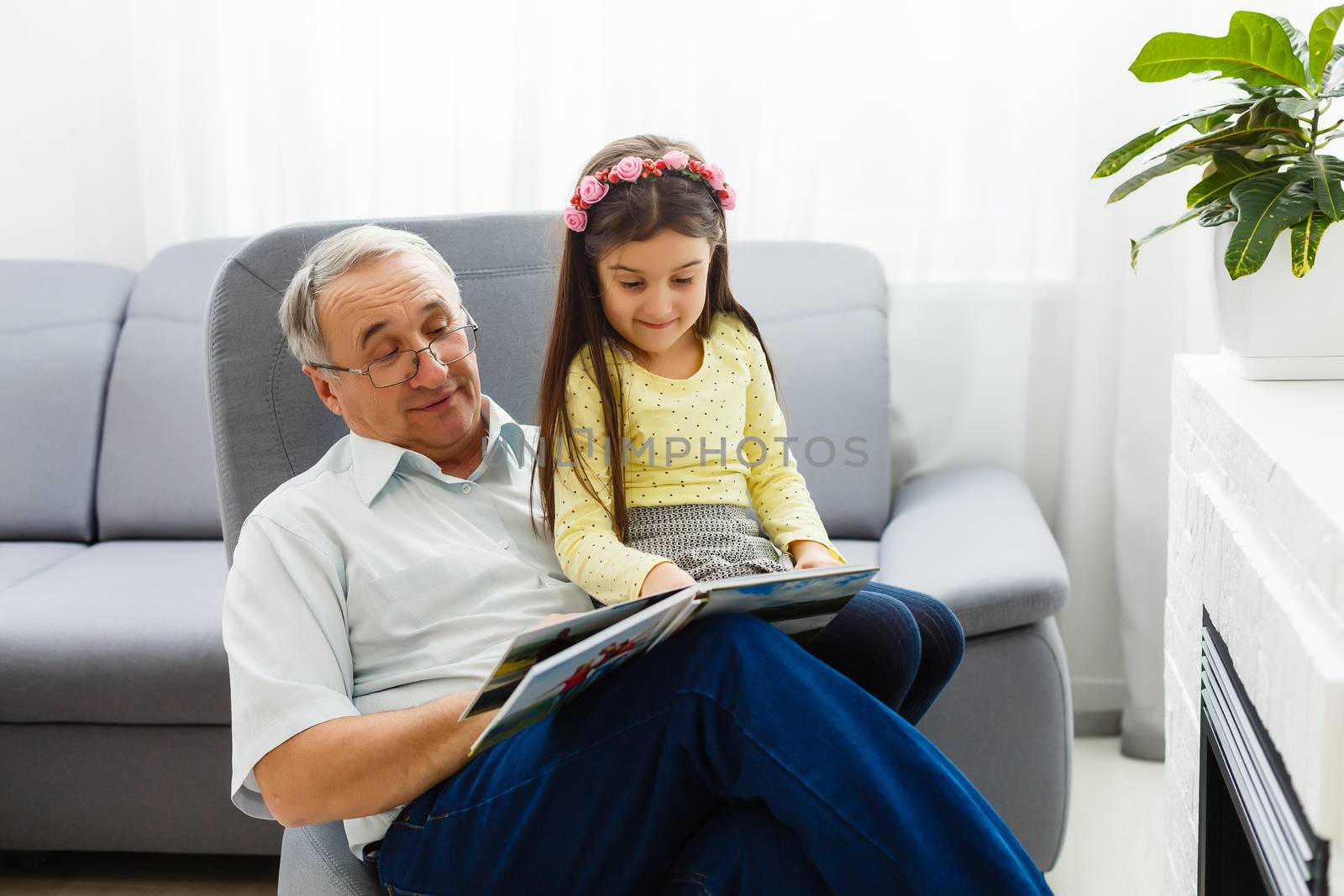 Granddaughter and grandfather watching photos together in a photo album at home