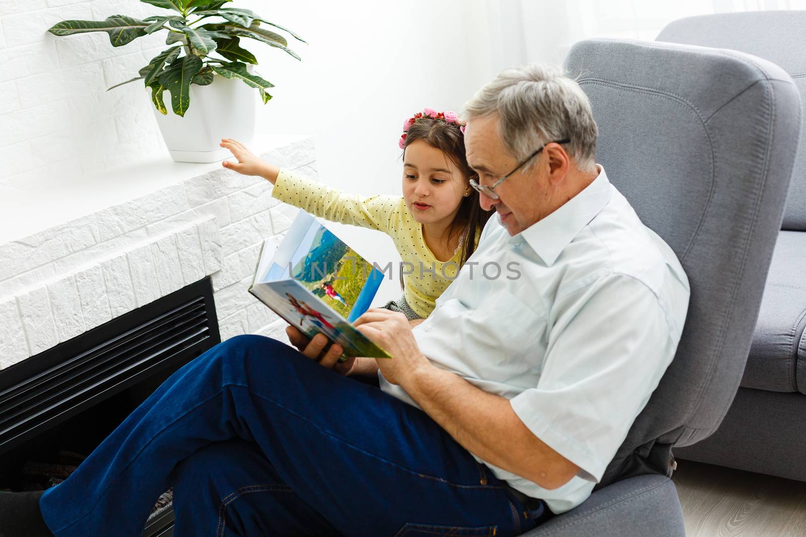 Granddaughter and grandfather watching photos together in a photo album at home by Andelov13