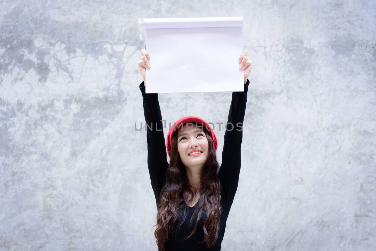 Asian woman with red hat and black clothes has holding a white paper on the grey stone wallpaper background with copy space.