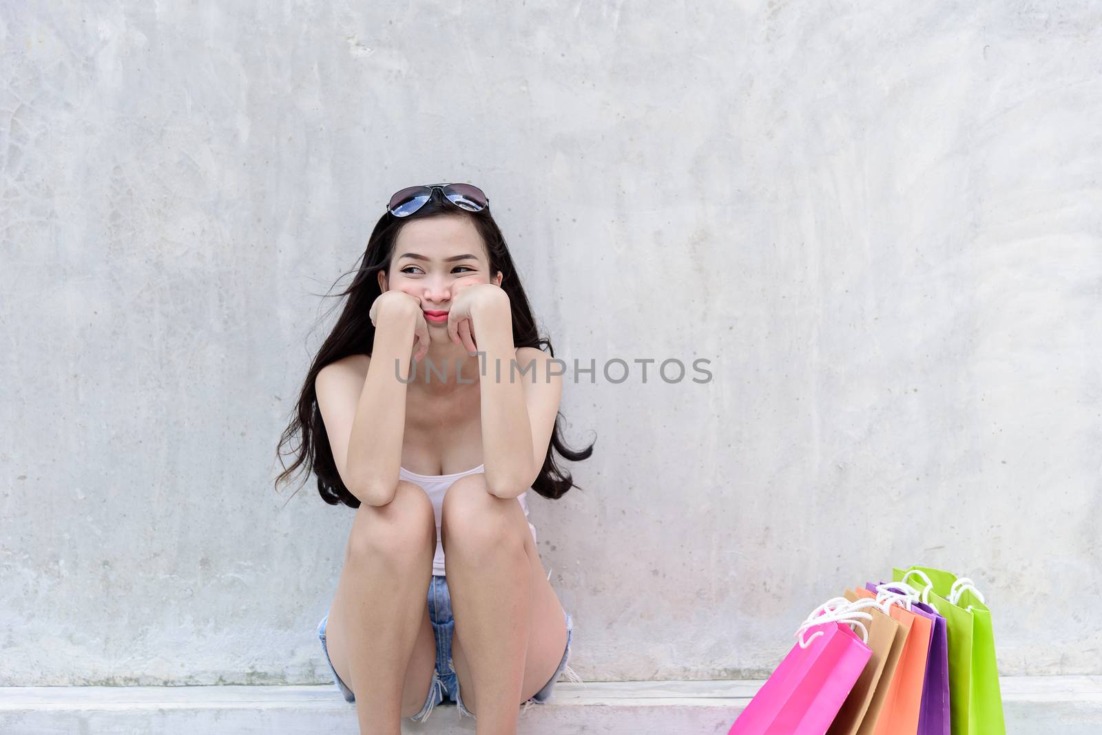 Asian fashion woman has sad, unhappy and tired with shopping bags sitting on a sidewalk.