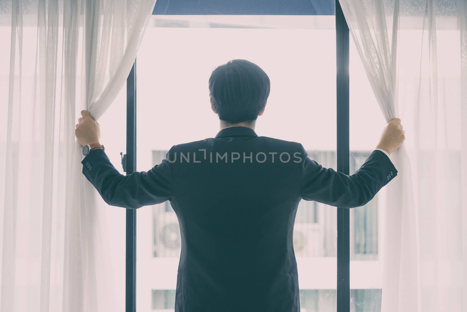 Asian manager businessman has opening window and curtain with feeling hopeful with lighting in the morning.