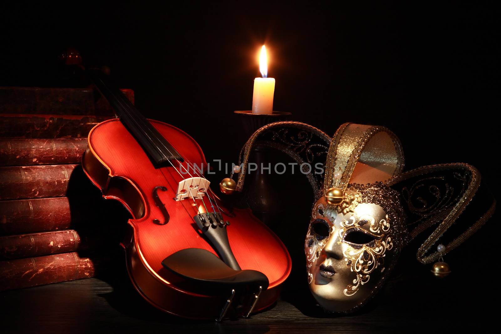 Nice violin near Venetian mask and candle against black background