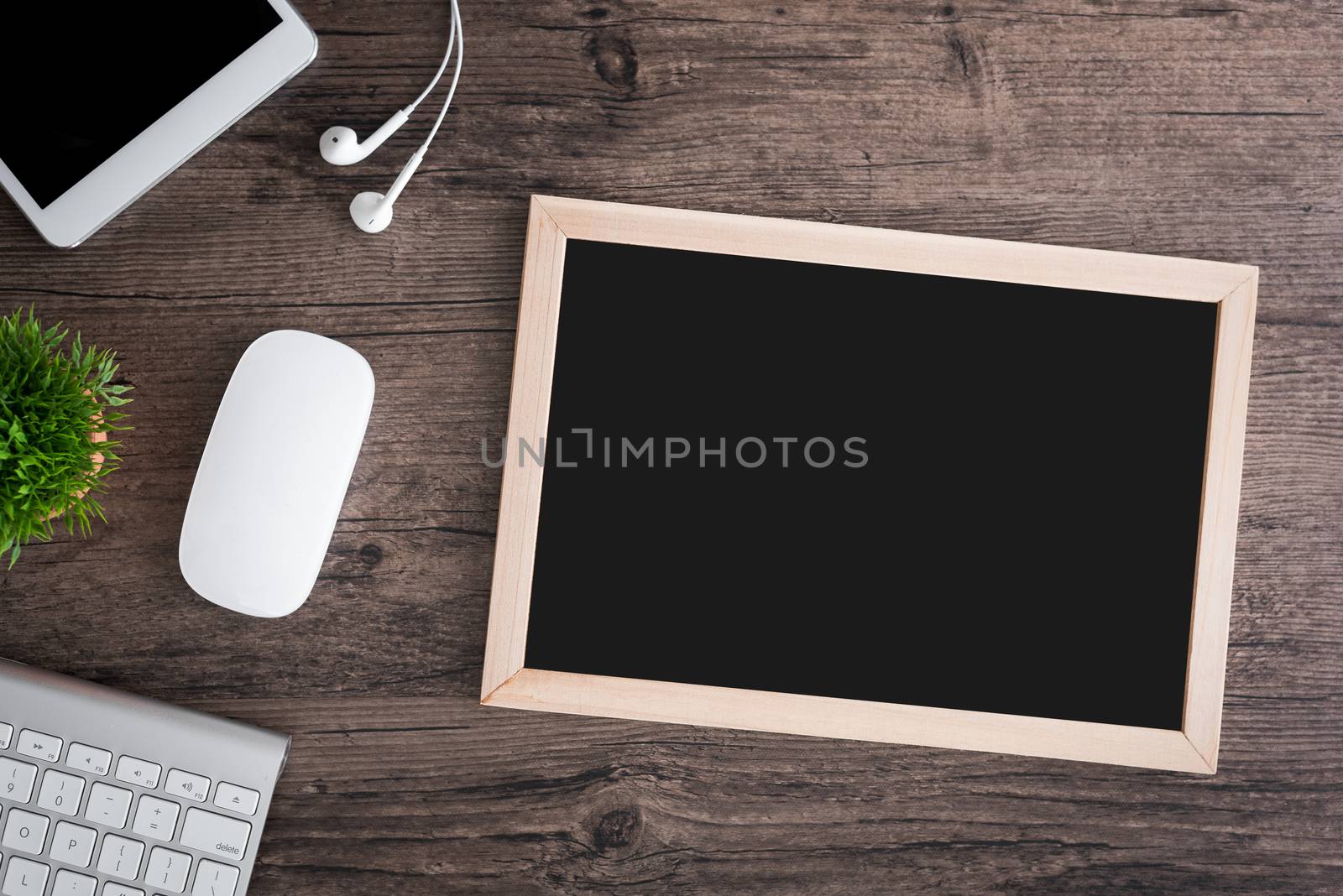 The office desk flat lay view with keyboard, mouse, tree, office pin board and earphone on wood texture background.