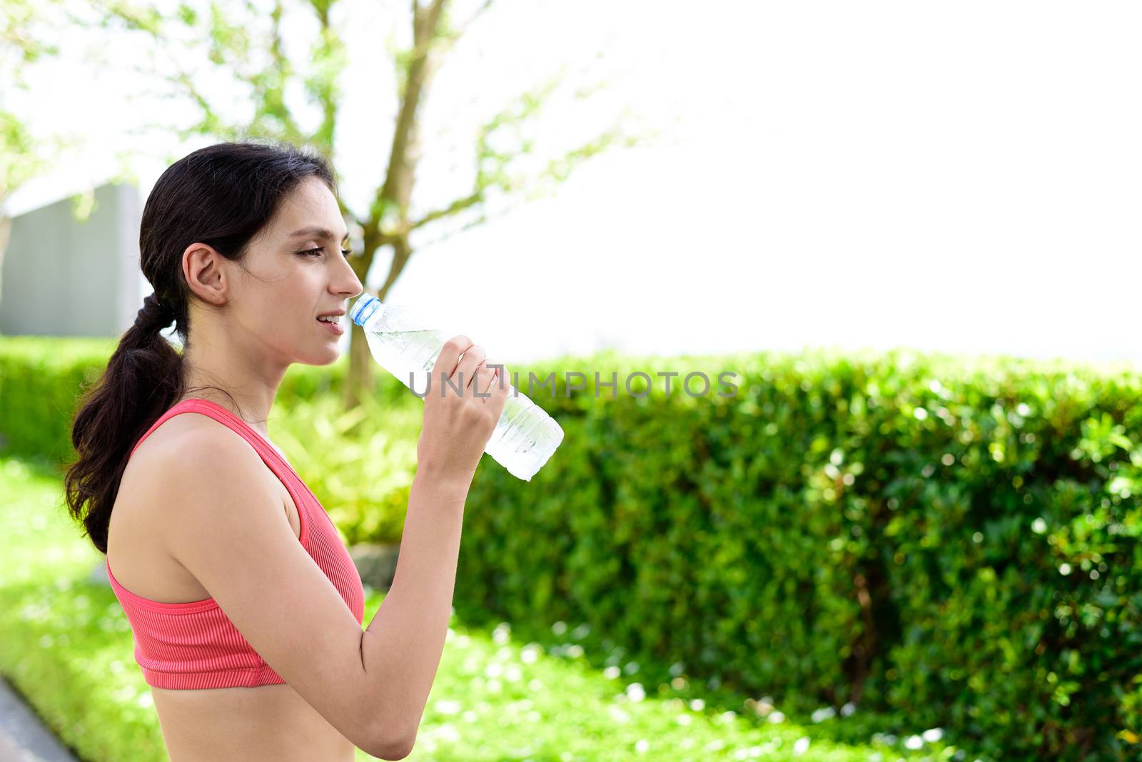 Beautiful woman runner has drinking water in the garden. by animagesdesign