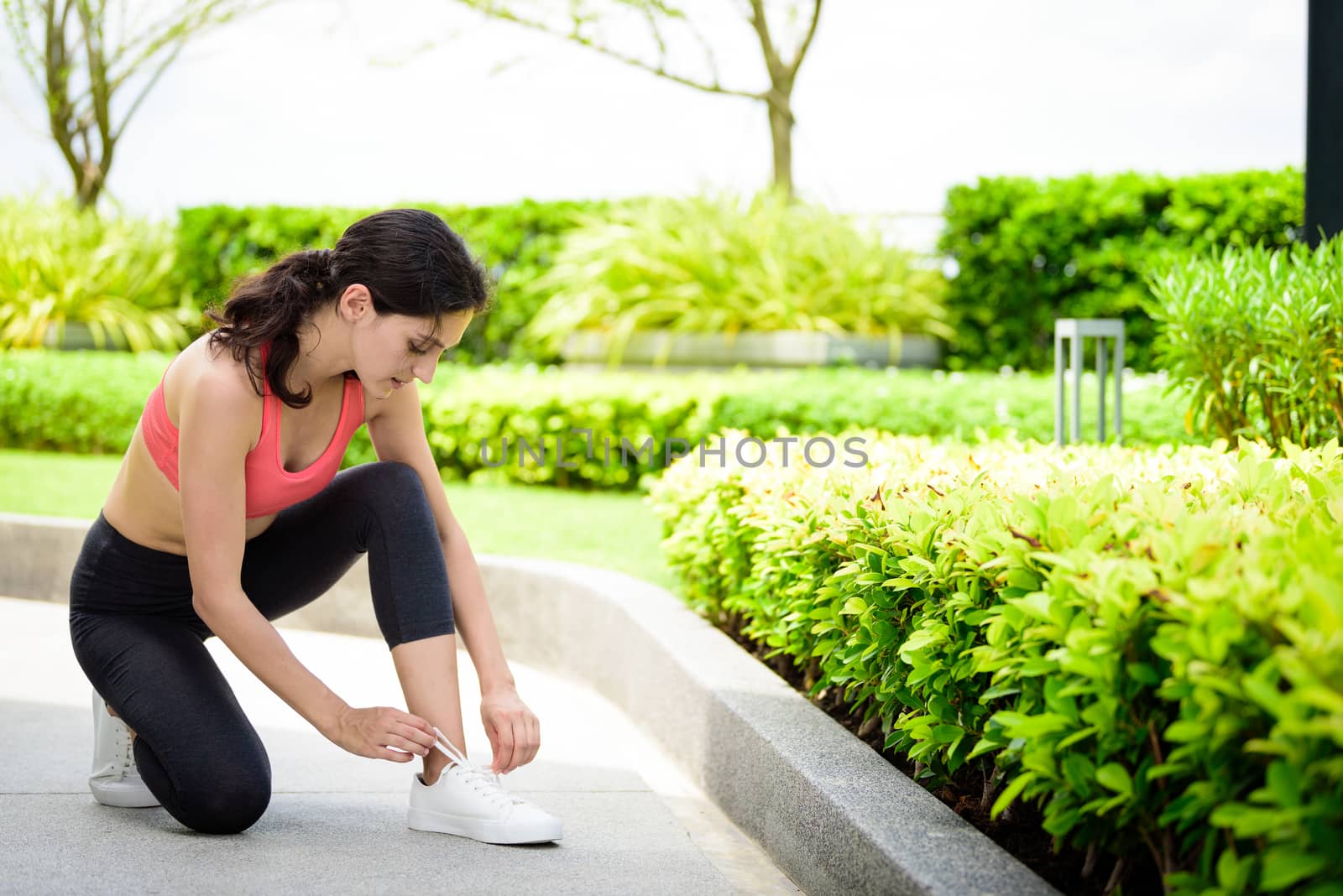 Beautiful woman runner has to tie white shoelaces in the garden. by animagesdesign