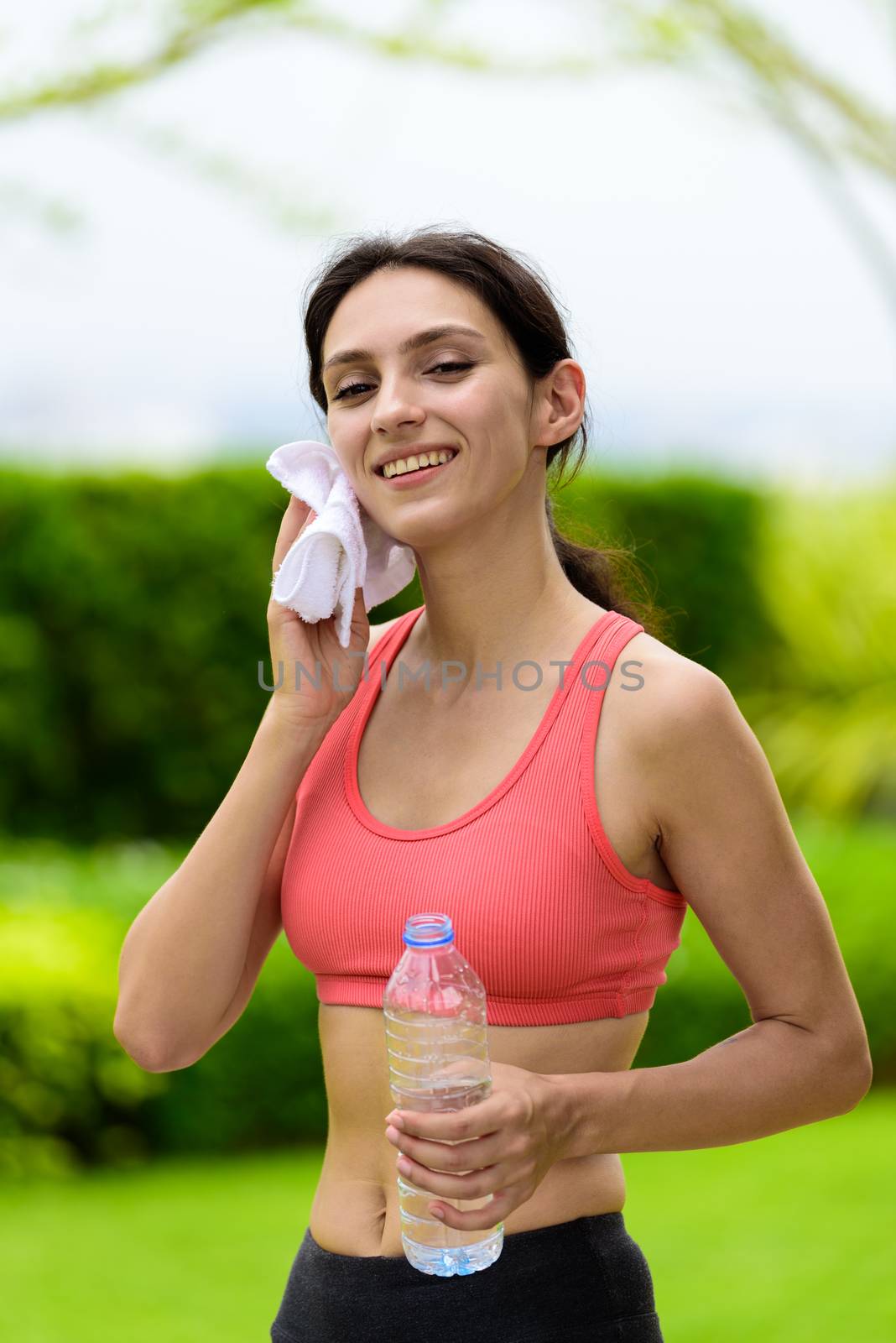 Beautiful woman runner has tired and rest for drinking water and a white towel to wipe her face after running in the garden.