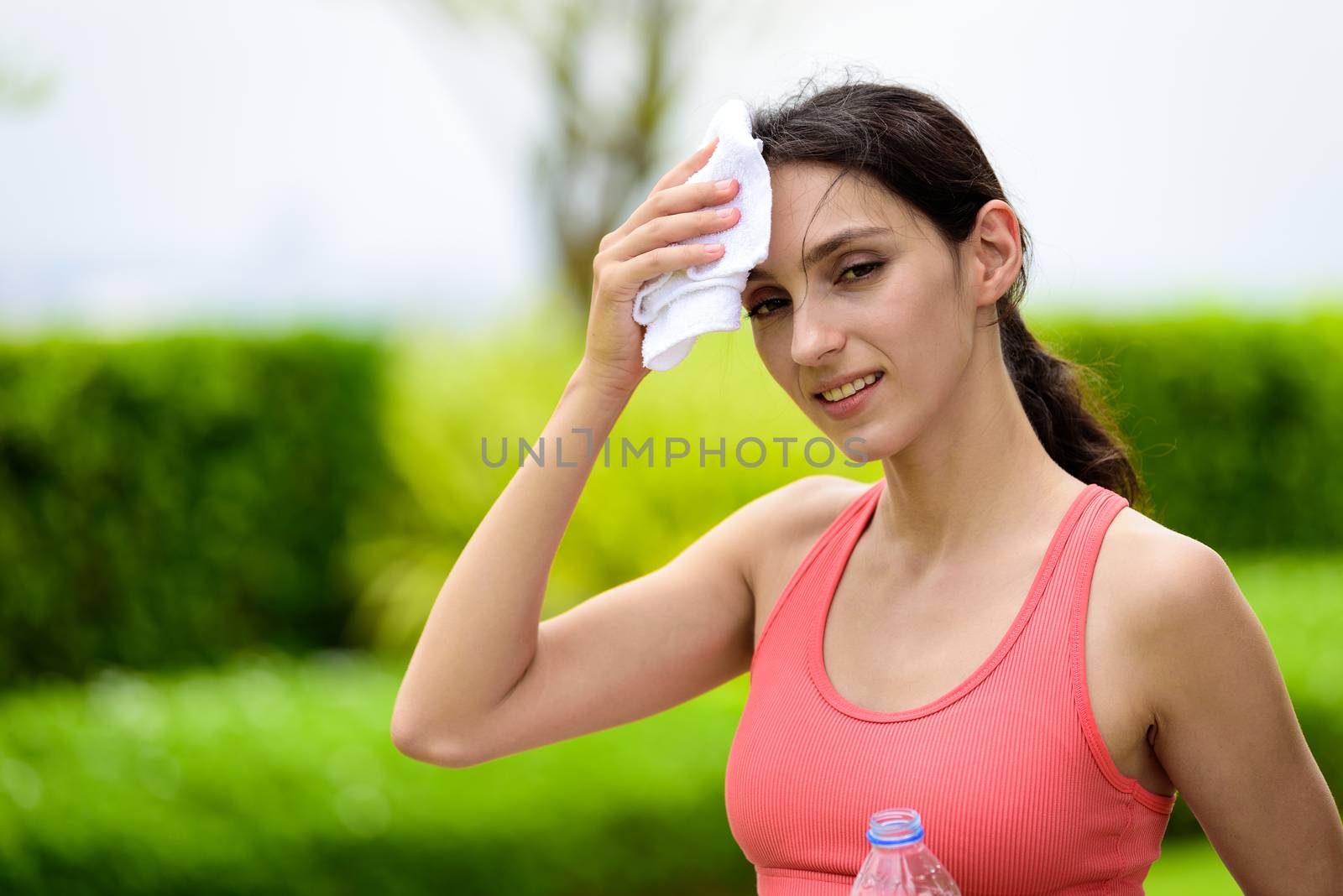 Beautiful woman runner has tired and rest for drinking water and a white towel to wipe her face after running in the garden.