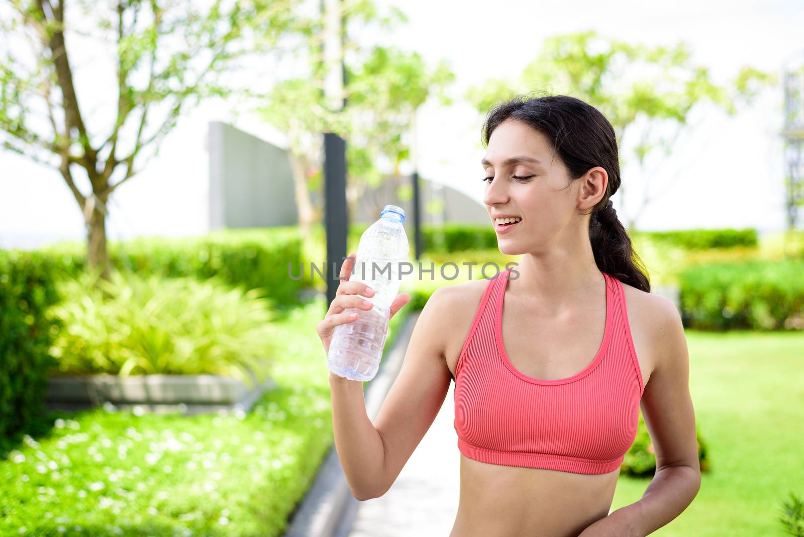 Beautiful woman runner has drinking water in the garden. by animagesdesign