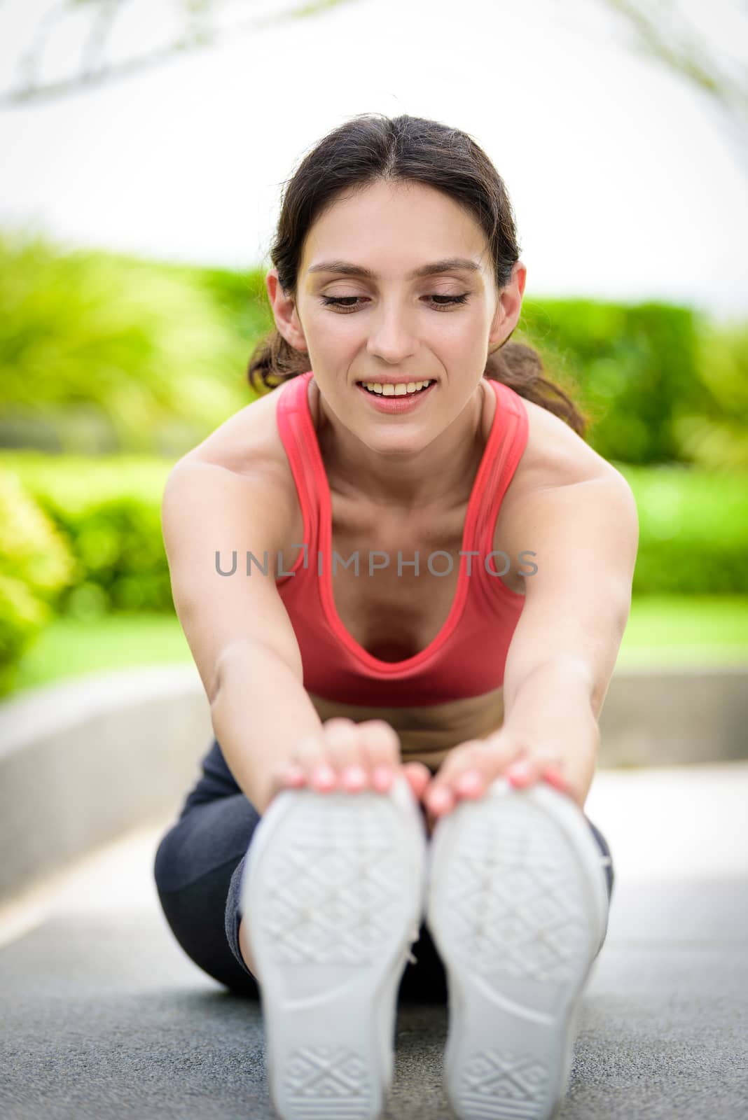 Beautiful woman runner has to warm up with stretching in the garden.