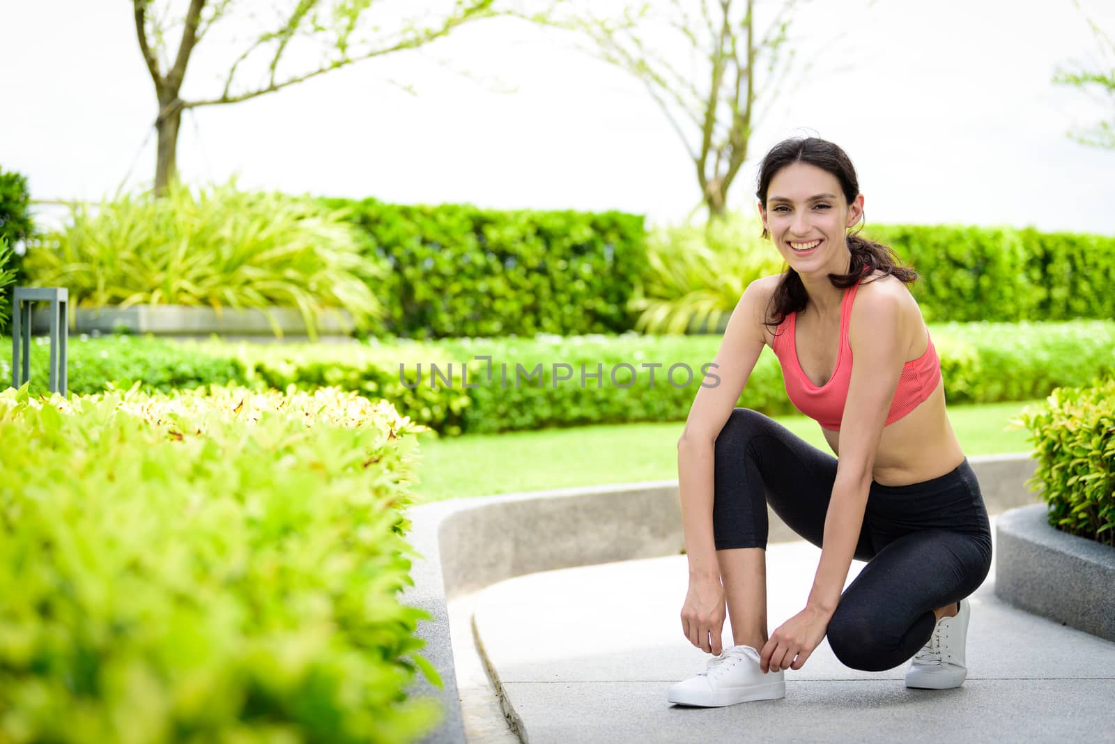 Beautiful woman runner has to tie white shoelaces in the garden.