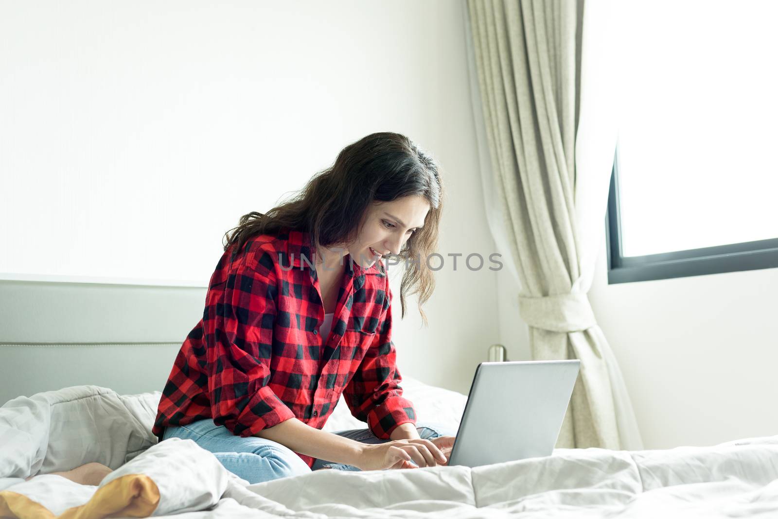 Beautiful woman working on a laptop with smiling and sitting on the bed at a condominium in the morning.