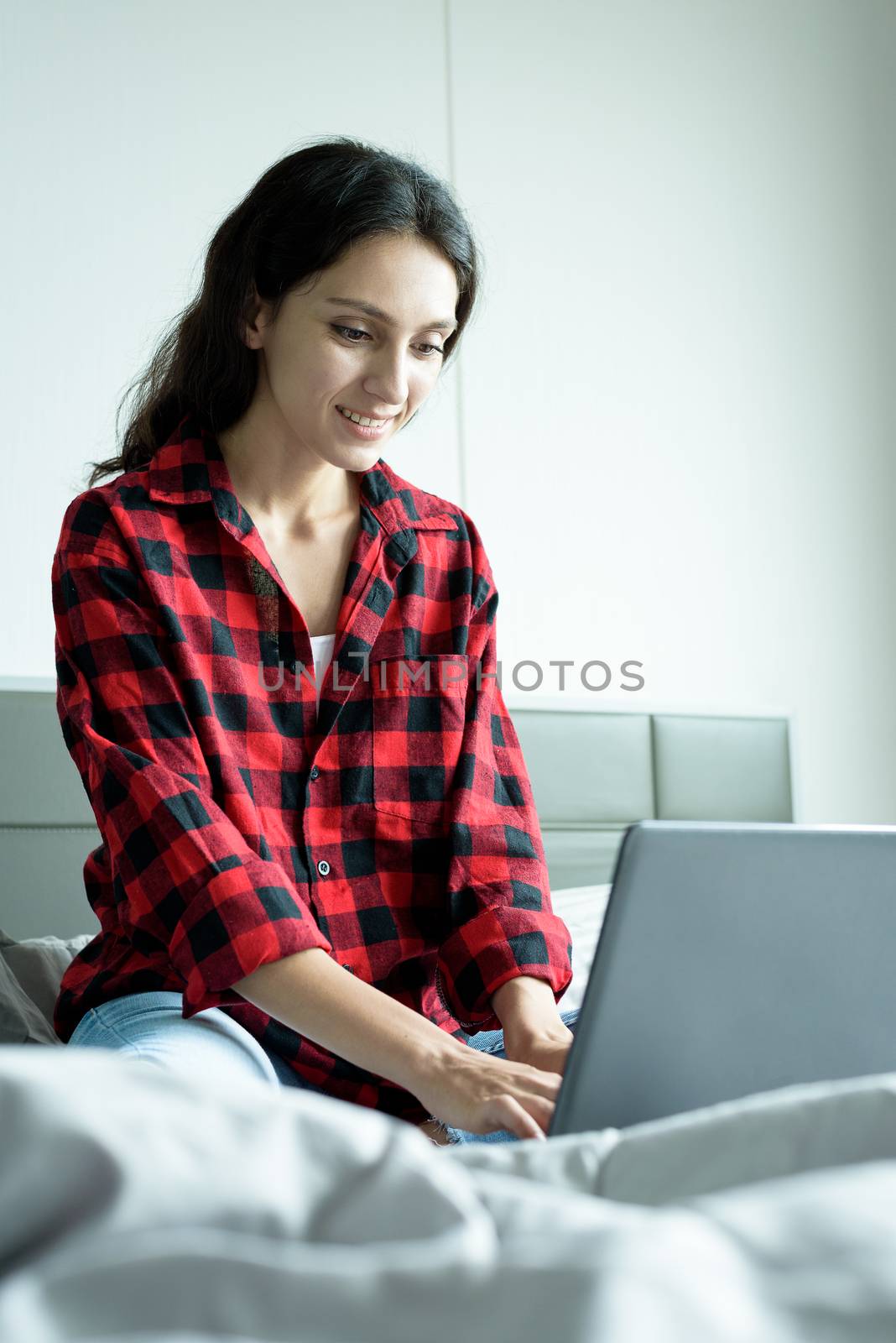 Beautiful woman working on a laptop with smiling and sitting on the bed at a condominium in the morning.