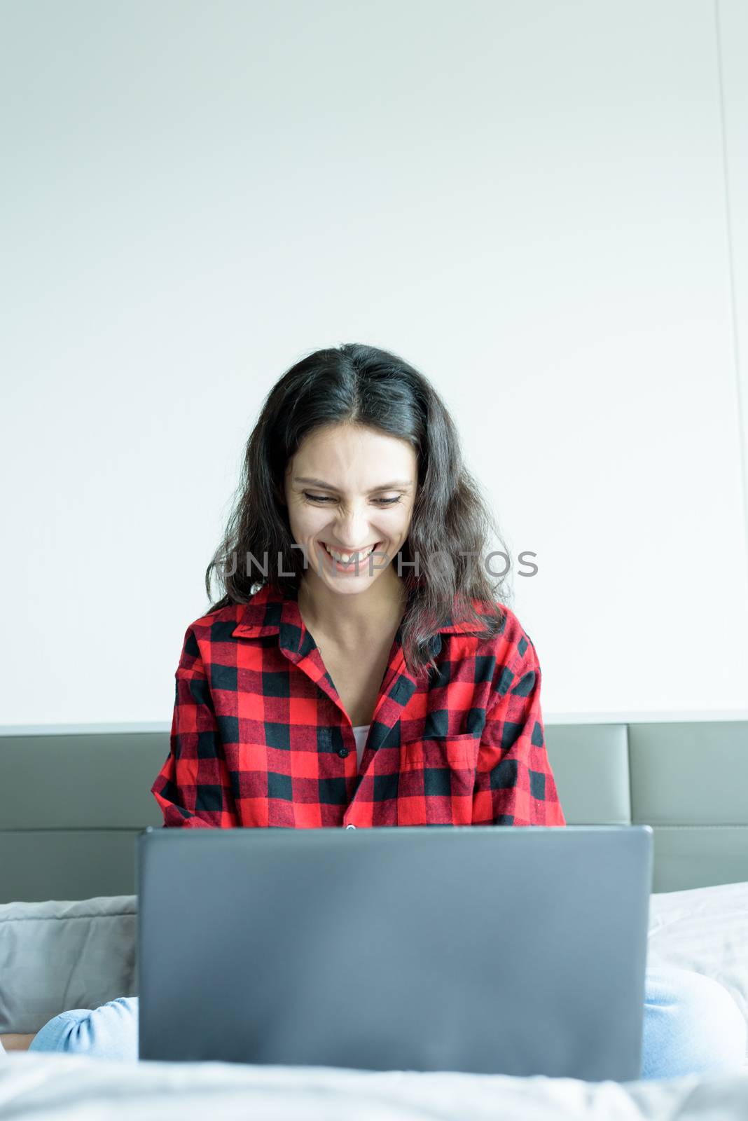 Beautiful woman working on a laptop with smiling and sitting on the bed at a condominium in the morning.