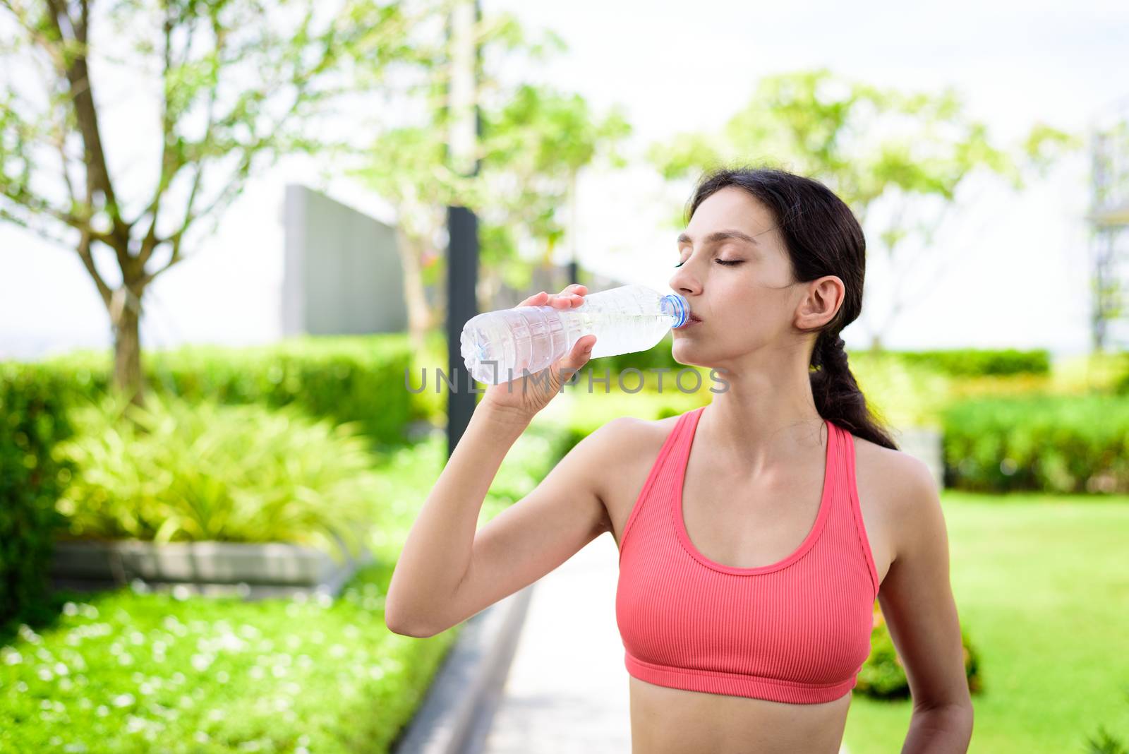 Beautiful woman runner has drinking water in the garden. by animagesdesign