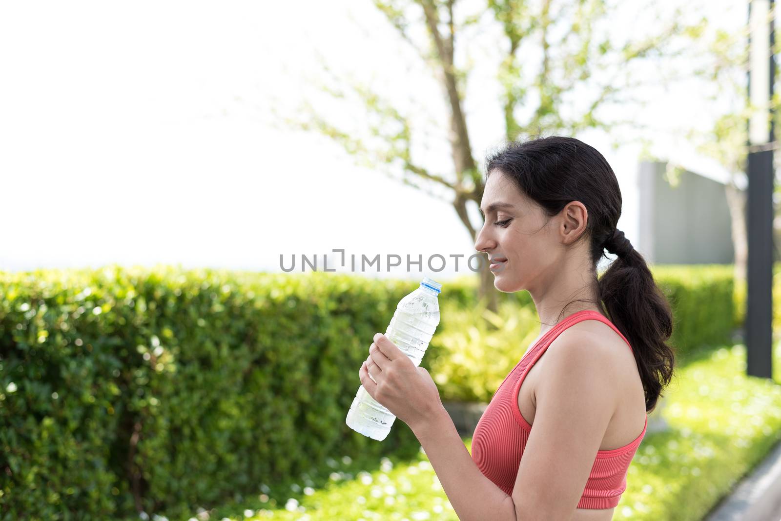Beautiful woman runner has drinking water in the garden. by animagesdesign